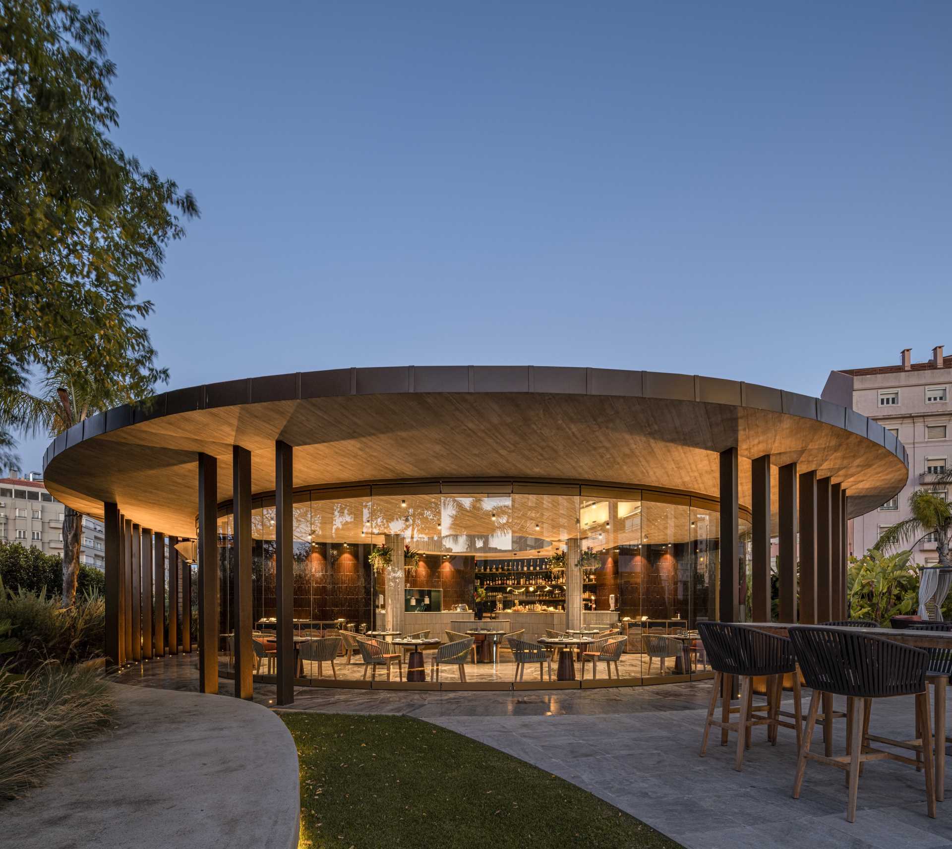 A hotel bar with a curved design has glass walls that open to the surrounding terrace.