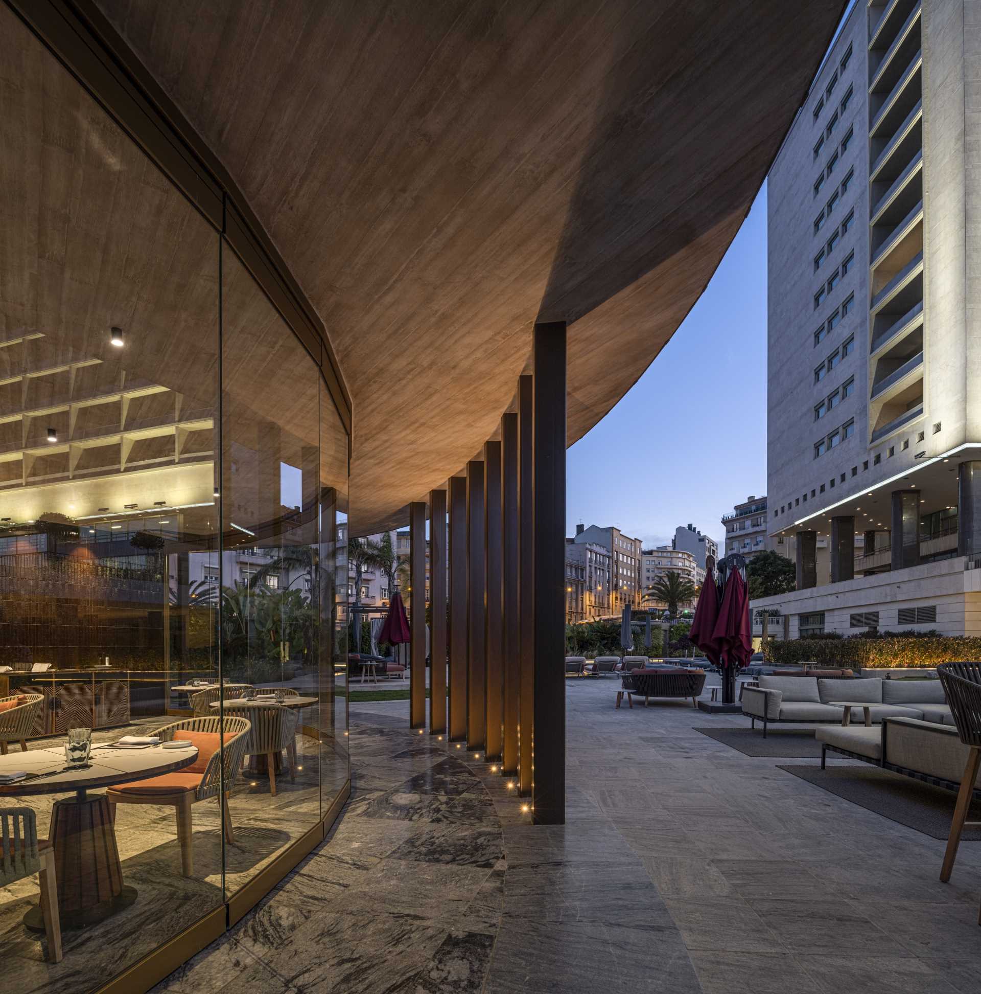 A hotel bar with a curved design has glass walls that open to the surrounding terrace.