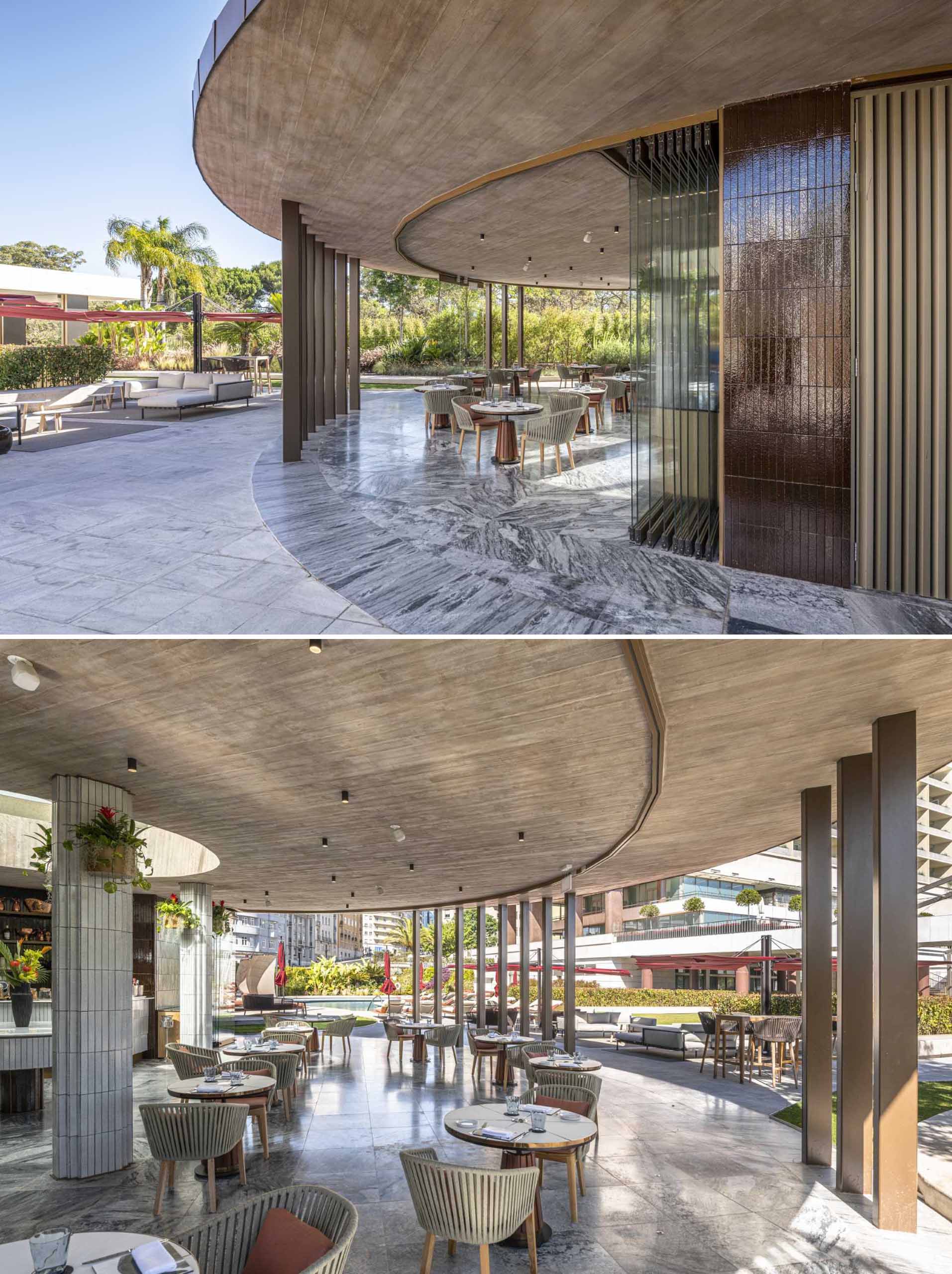 A hotel bar with a curved design has glass walls that open to the surrounding terrace.