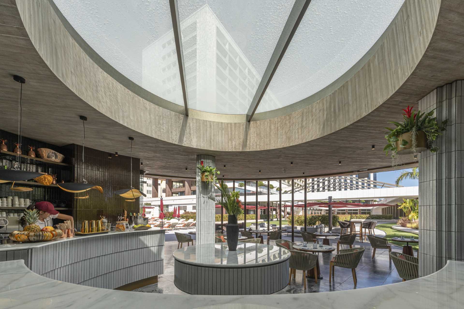 A hotel bar with a curved design has glass walls that open to the surrounding terrace.