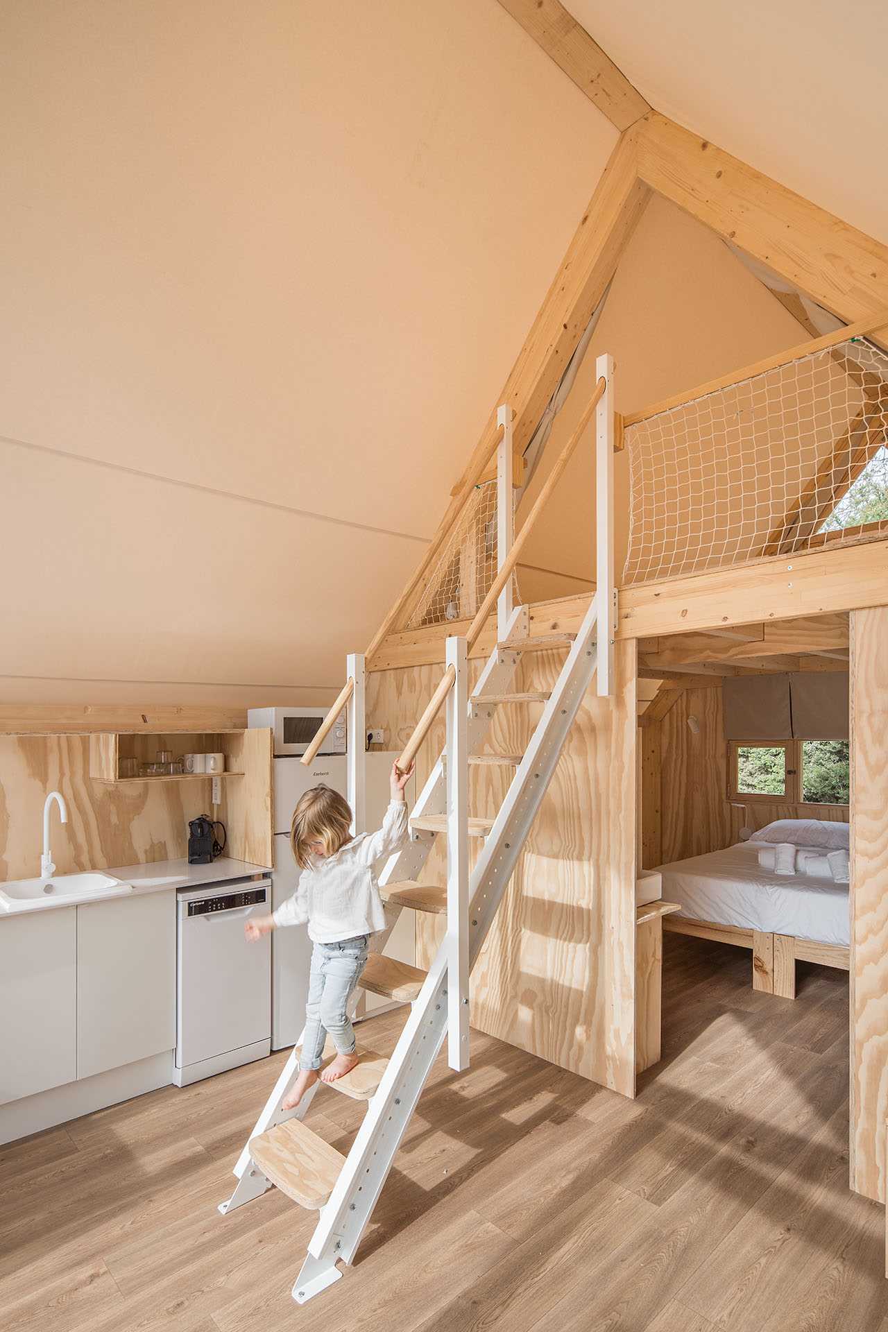 A modern glamping tent with a living room, kitchen, main bedroom, bathroom, and second lofted bedroom.