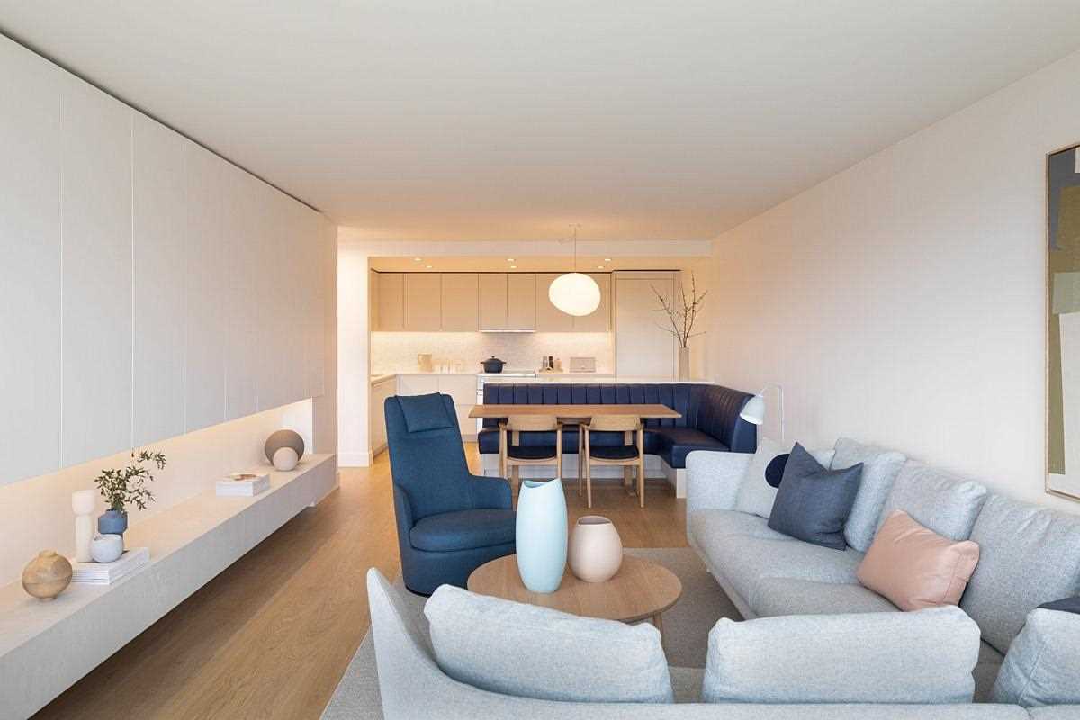 A dining area includes a built-in banquette between the living room and kitchen that features a pop of color in the form of navy leather seating that curves around from the peninsula to the wall.