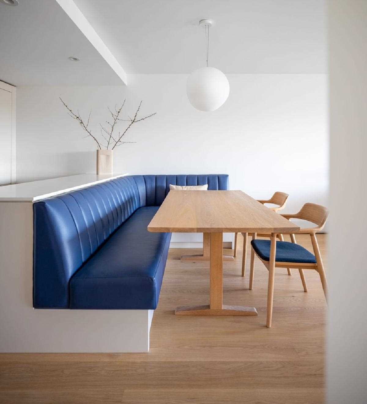 A dining area includes a built-in banquette between the living room and kitchen that features a pop of color in the form of navy leather seating that curves around from the peninsula to the wall.