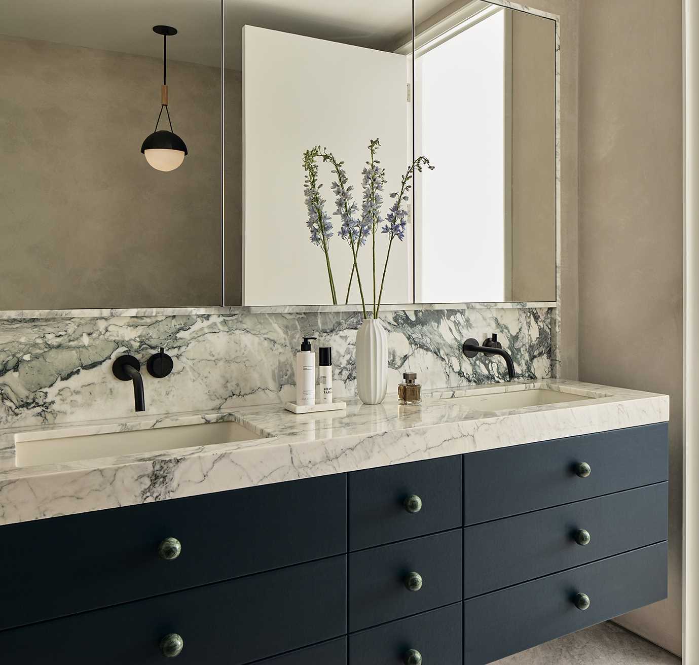 This modern bathroom has an earthy interior with stone accents and a matte black bathtub.