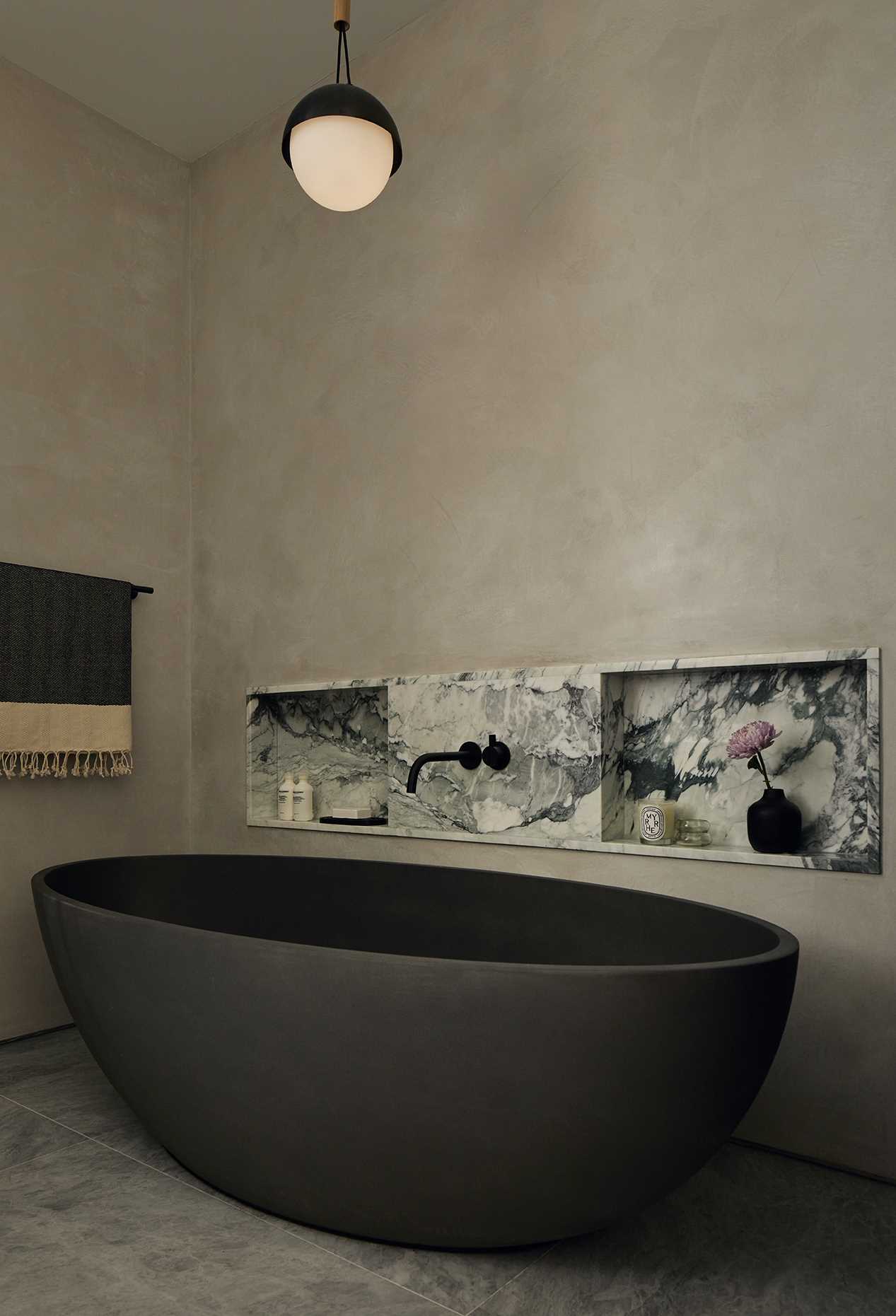 This modern bathroom has an earthy interior with stone accents and a matte black bathtub.