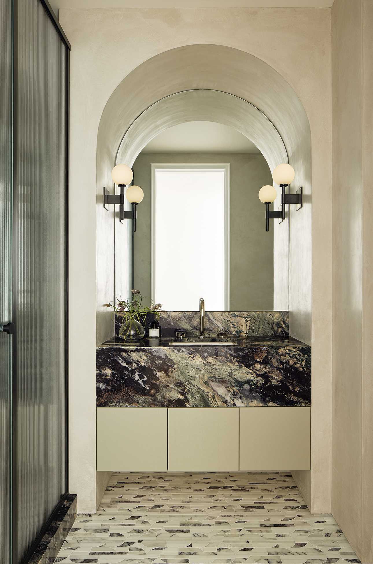 In this bathroom, an arched mirror follows the curve of the wall, while the floor tiles add a subtle pattern, which flows through to the shower.