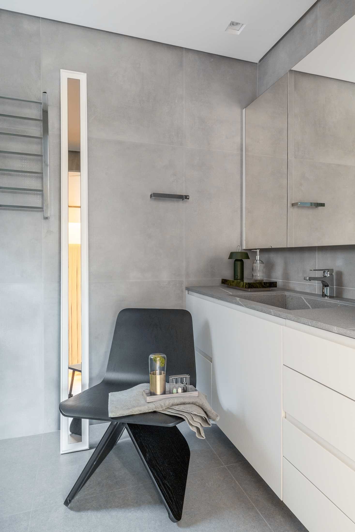 In this bathroom, large format grey tiles line the walls and floor, providing a contrasting element to the white vanity and closets.