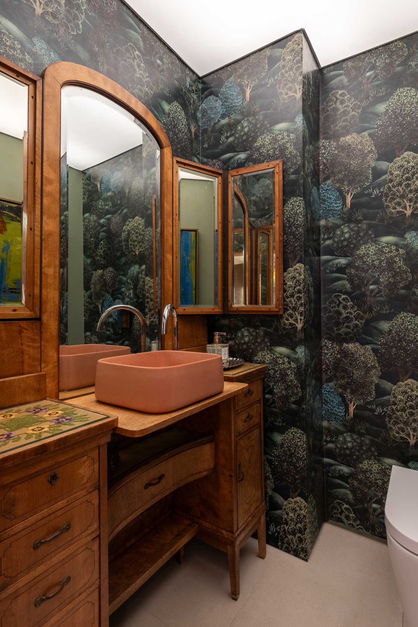 A contemporary bathroom with a antique wood vanity and a forest wallpaper.