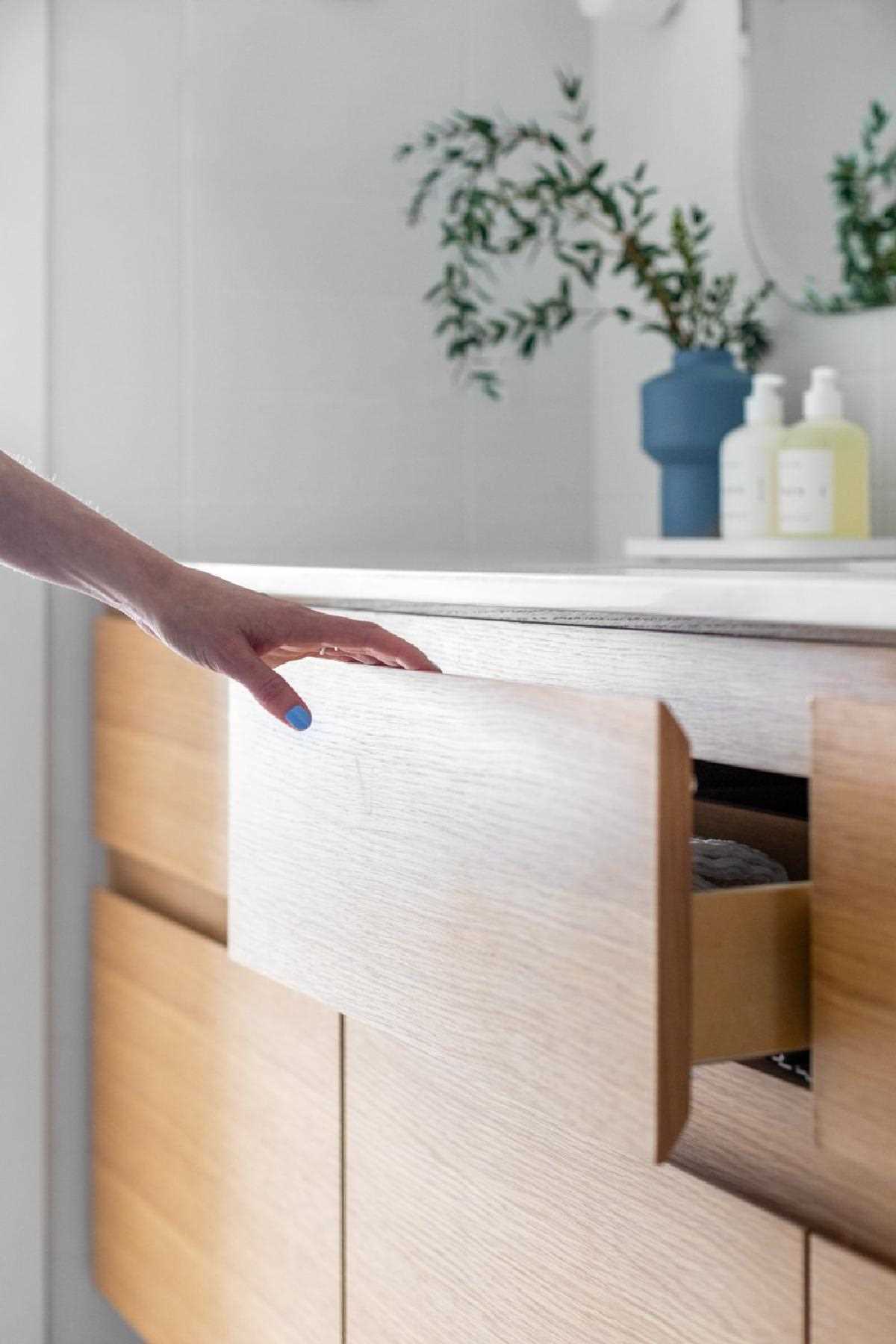 In the bathroom, the Terrazzo tiles make another appearance on the floor, complementing the tiles in the kitchen. A wood vanity adds a natural element and ties in with the bed frame seen through the doorway.