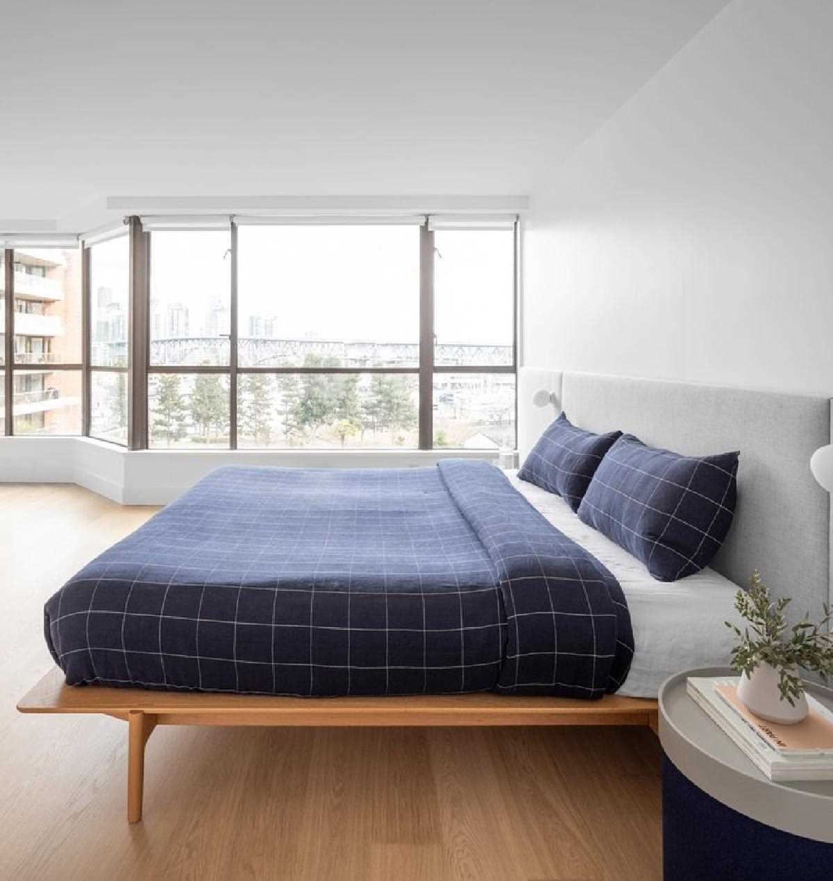 In this modern bedroom, a wall of windows fills the space with natural light, while the upholstered headboard spans the width of the wall.