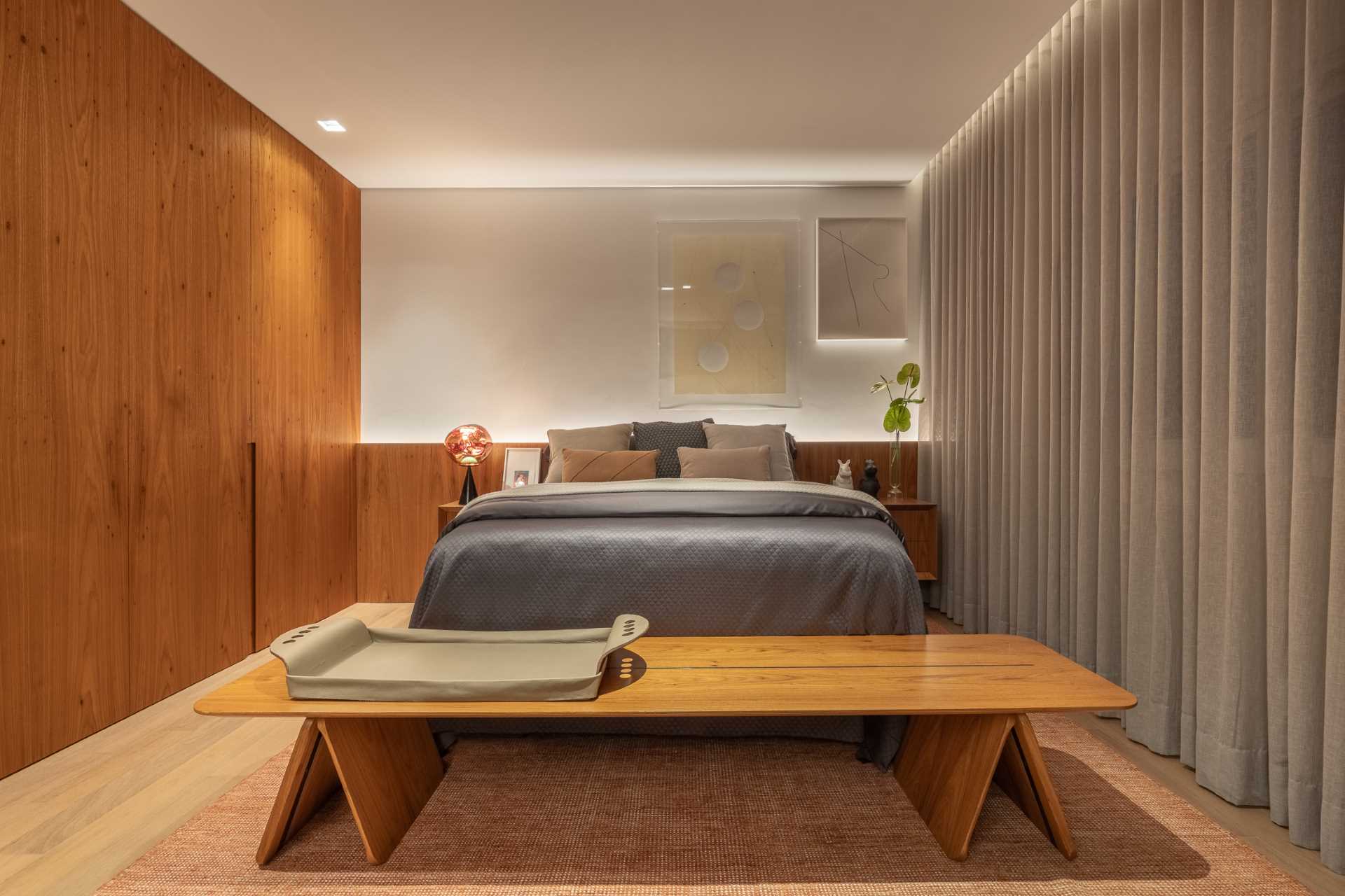 A modern bedroom with hidden lighting, a wood headboard, and wall of cabinets.