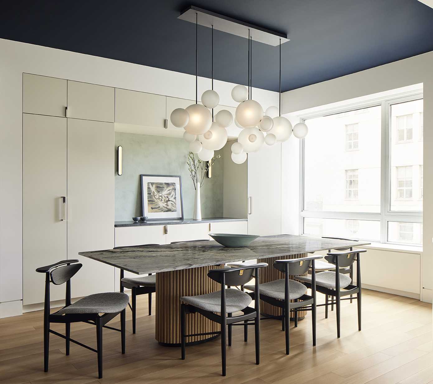 In the open-plan dining area, there's a dining table custom-designed by FTA in quartzite platinum crystal stone from Bas Stone. A sculptural Bolle chandelier in frosted glass and blackened metal from Giopato & Coombes floats above the dining table, like clouds, and the tambour-like fluting at the base of the dining table also graces the base of the nearby kitchen island.