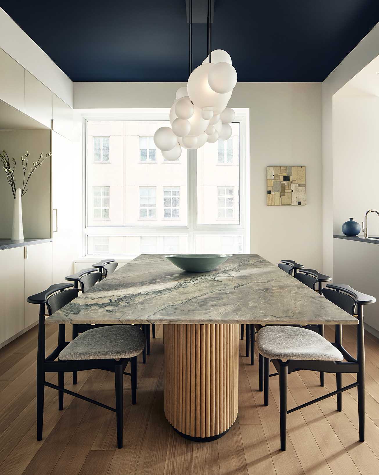 In the open-plan dining area, there's a dining table custom-designed by FTA in quartzite platinum crystal stone from Bas Stone. A sculptural Bolle chandelier in frosted glass and blackened metal from Giopato & Coombes floats above the dining table, like clouds, and the tambour-like fluting at the base of the dining table also graces the base of the nearby kitchen island.