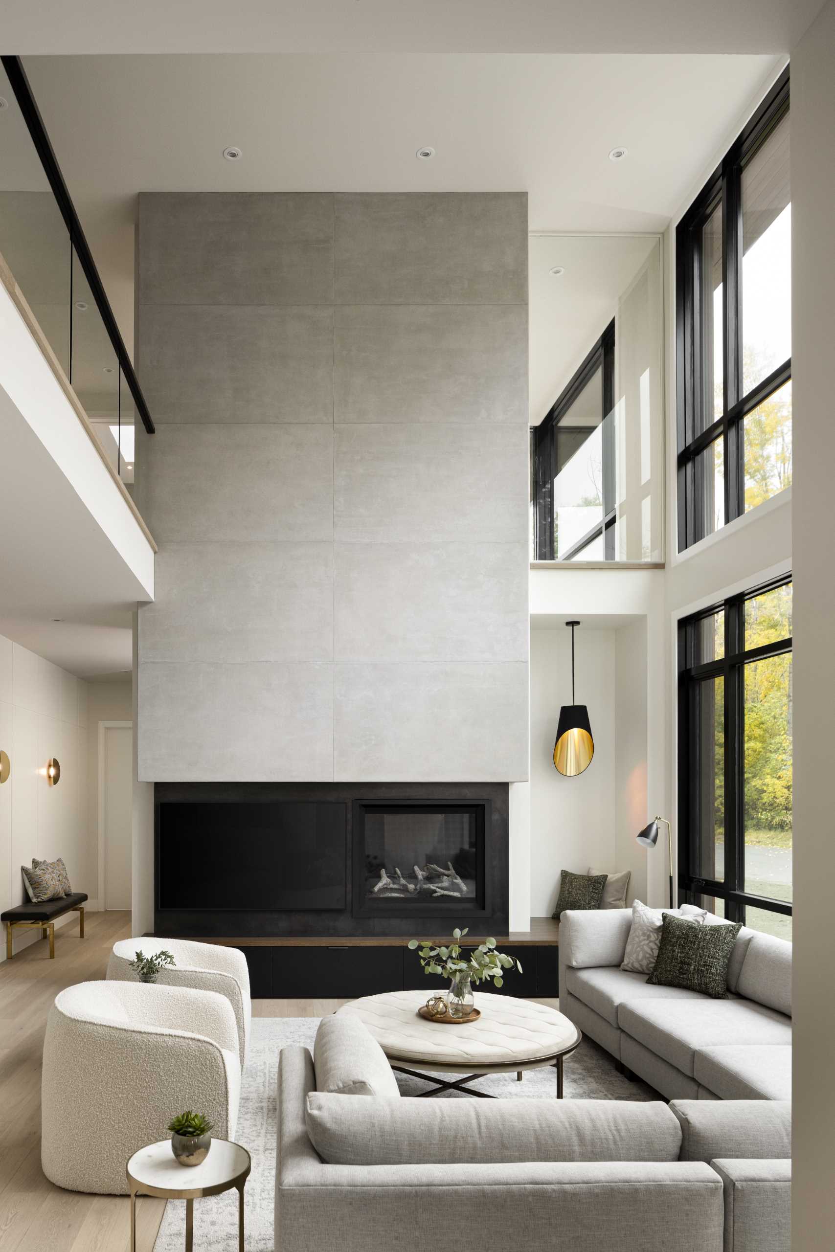 A modern living room with a fireplace has a double-height ceiling and a wall of windows.