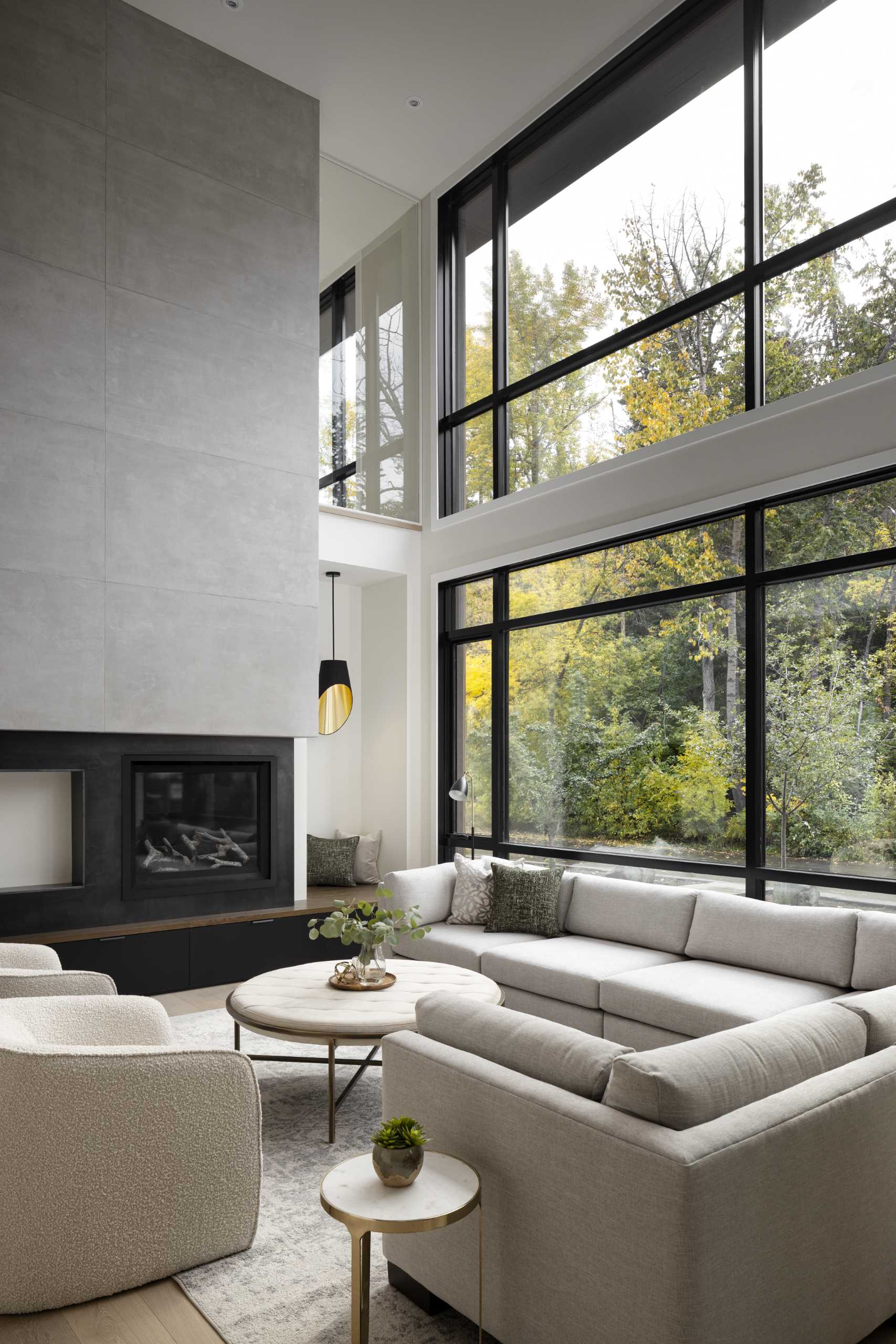 A modern living room with a fireplace has a double-height ceiling and a wall of windows.