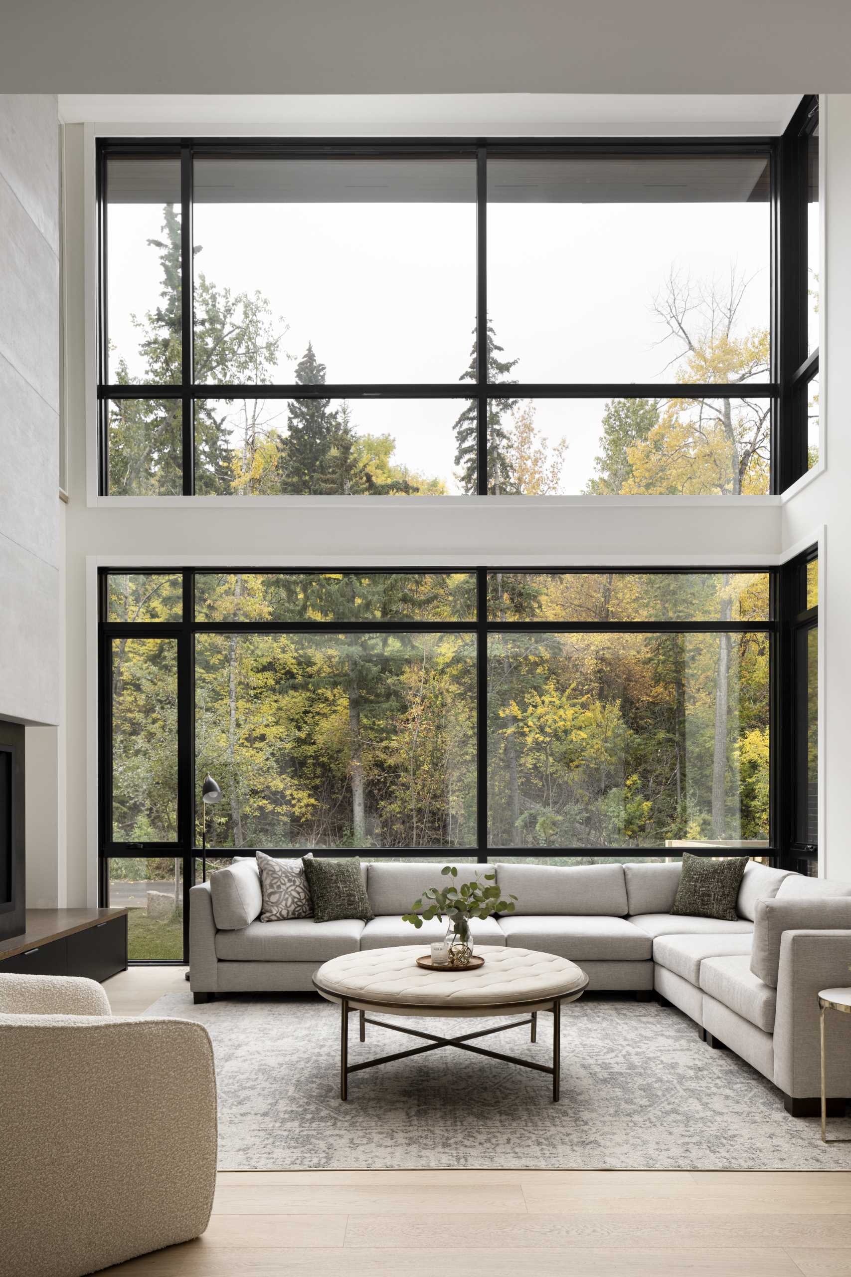 A modern living room with a fireplace has a double-height ceiling and a wall of windows.