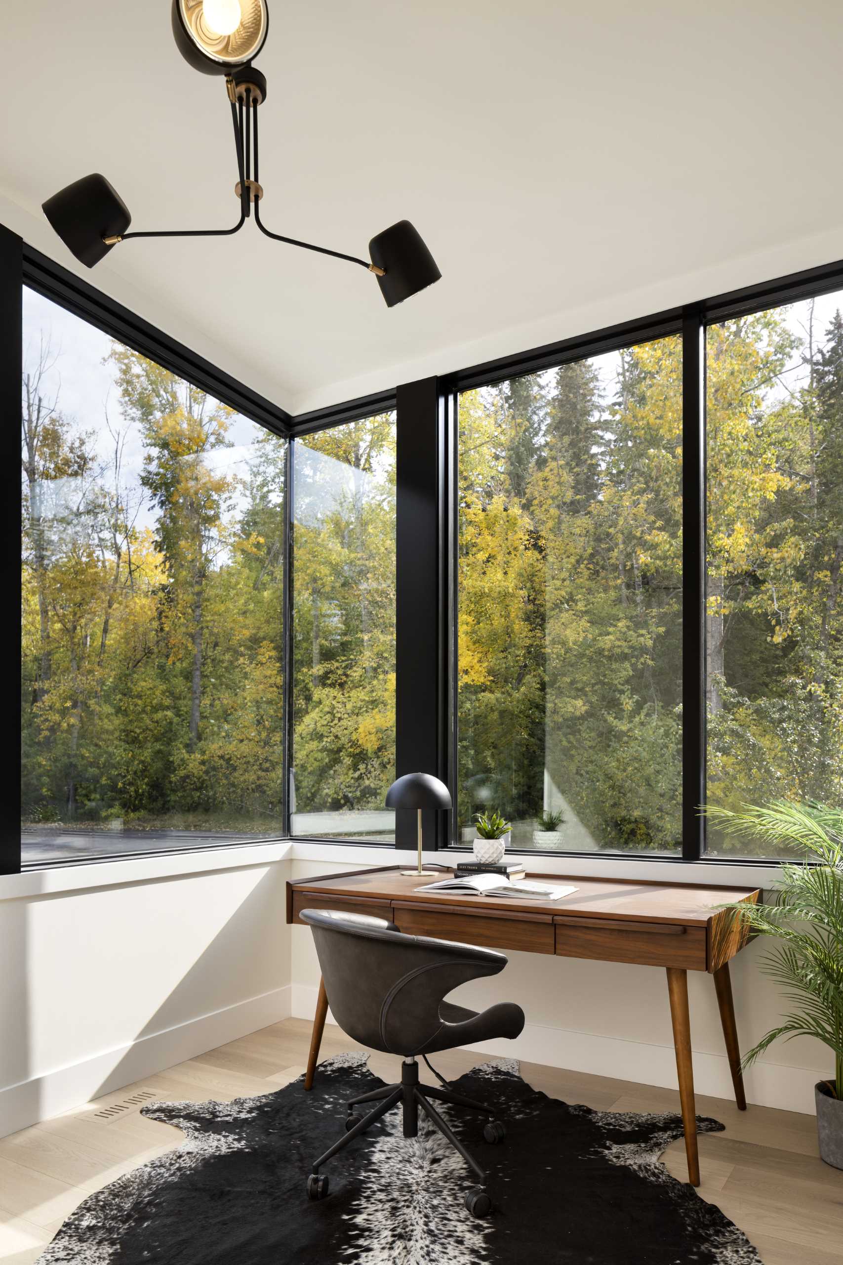 A modern home office with corner windows that provide an uninterrupted view of the forest.