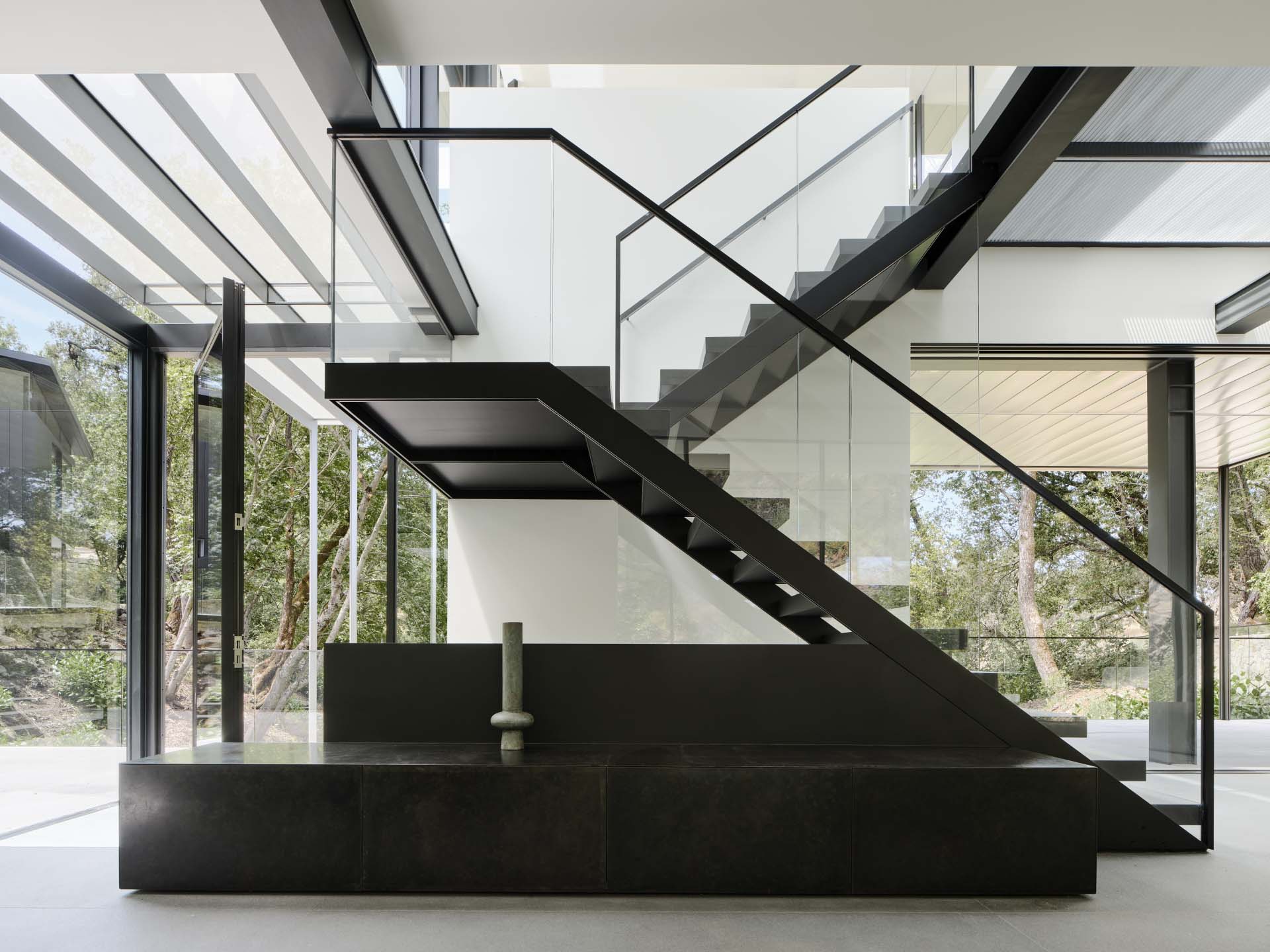 This interior black staircase, with its bold color and glass railings, acts as a sculpture in the space.