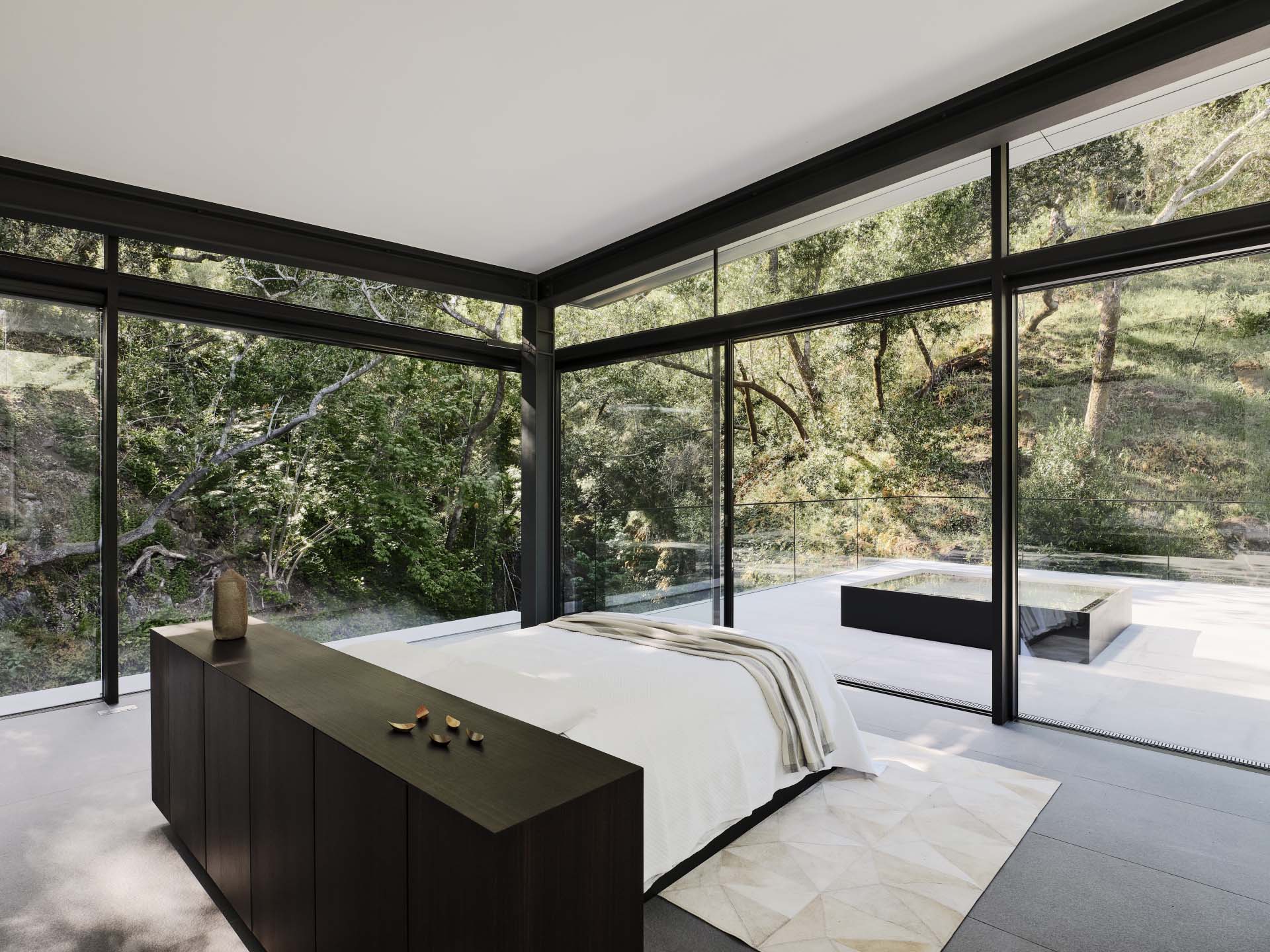 This primary bedroom has a bed located in the center of the room and looks out to the surrounding landscape.