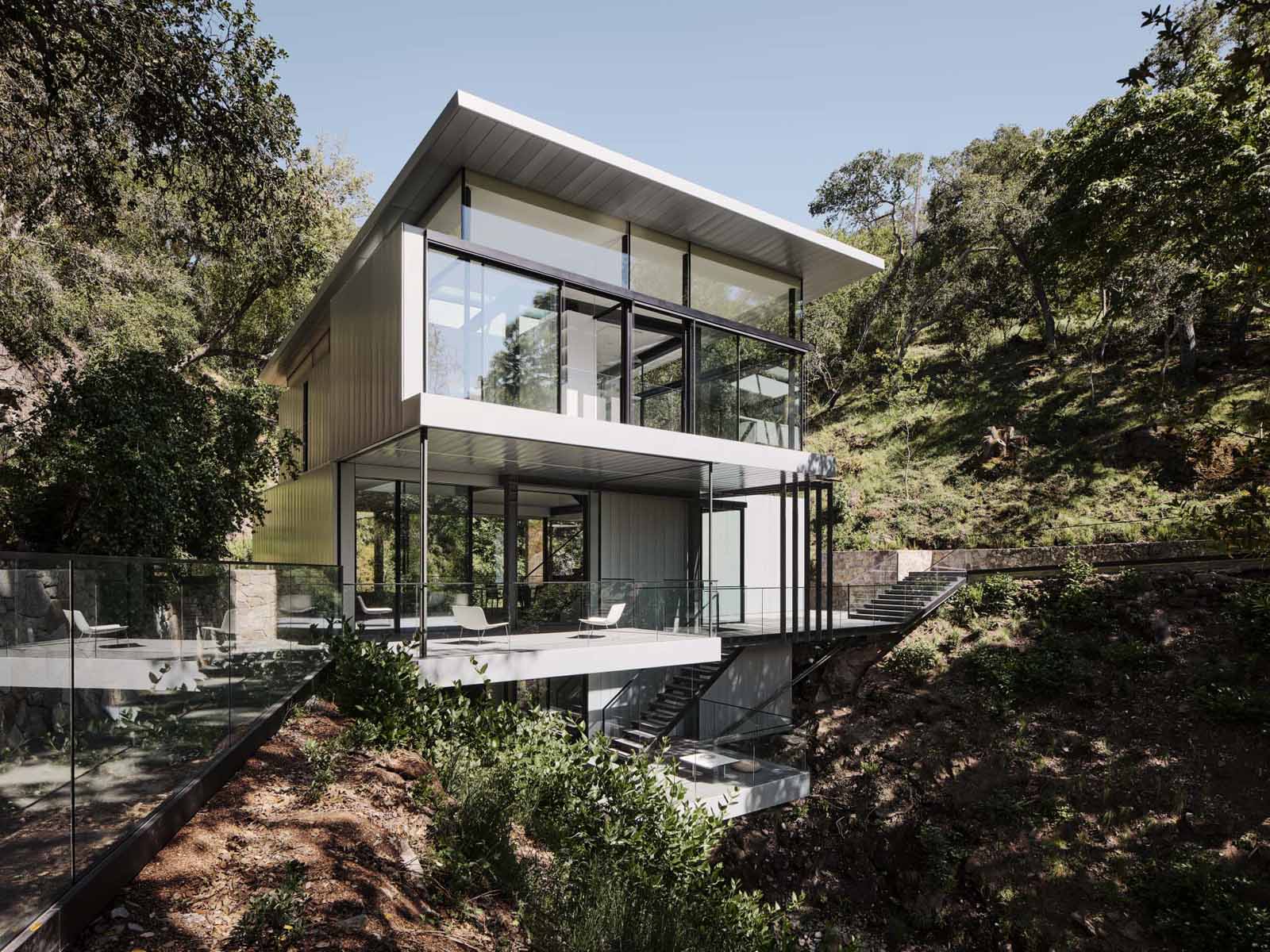 A modern home in California positioned between two hills and suspended over a creek.