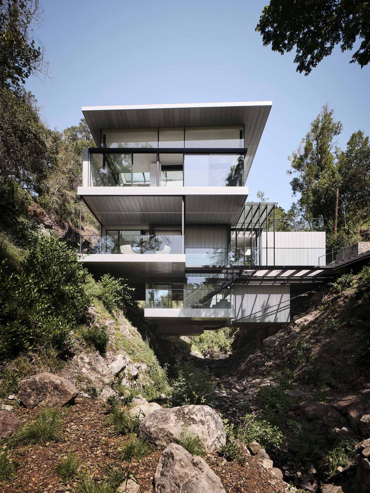 A modern home in California positioned between two hills and suspended over a creek.