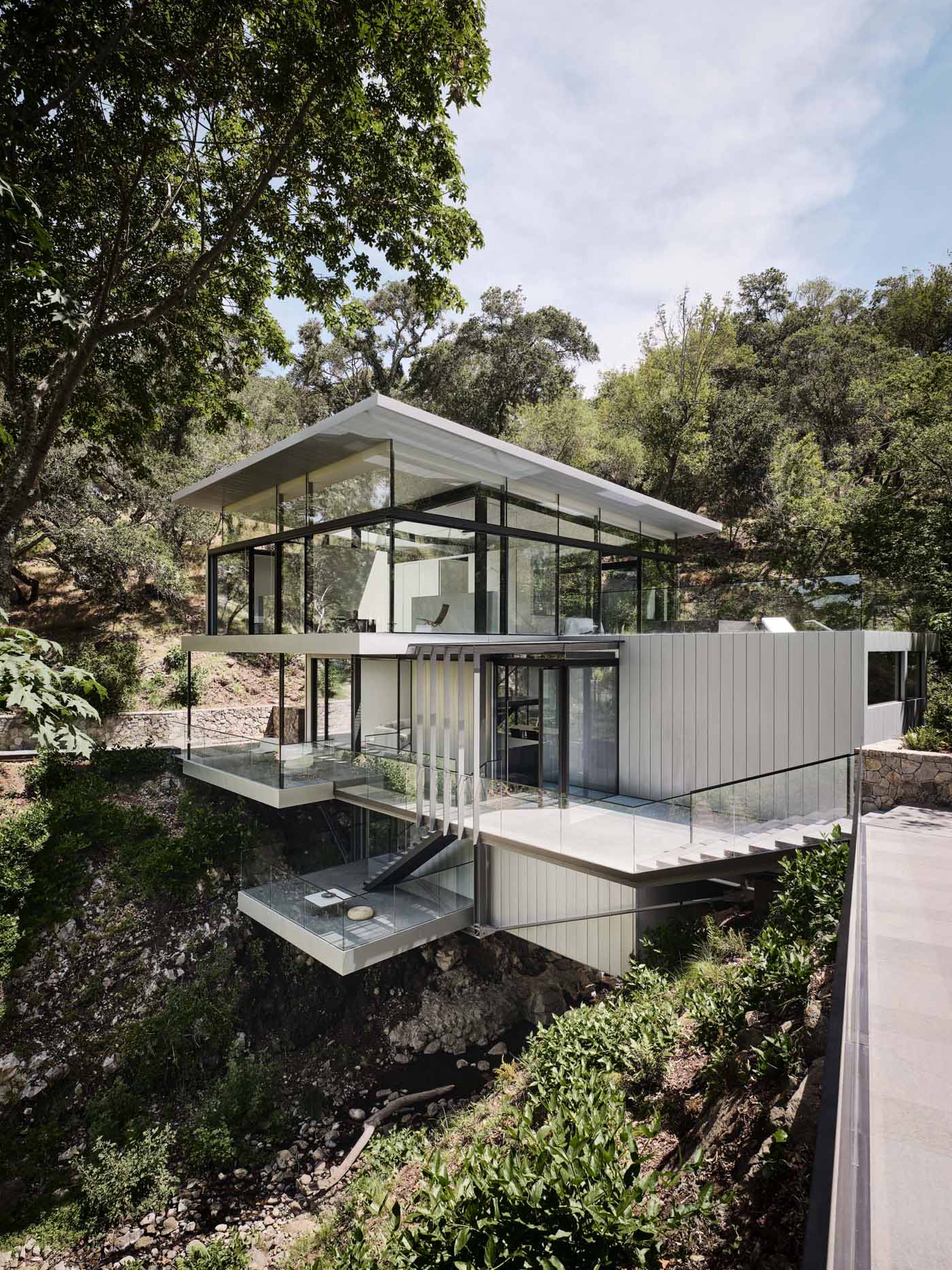 A modern home in California positioned between two hills and suspended over a creek.