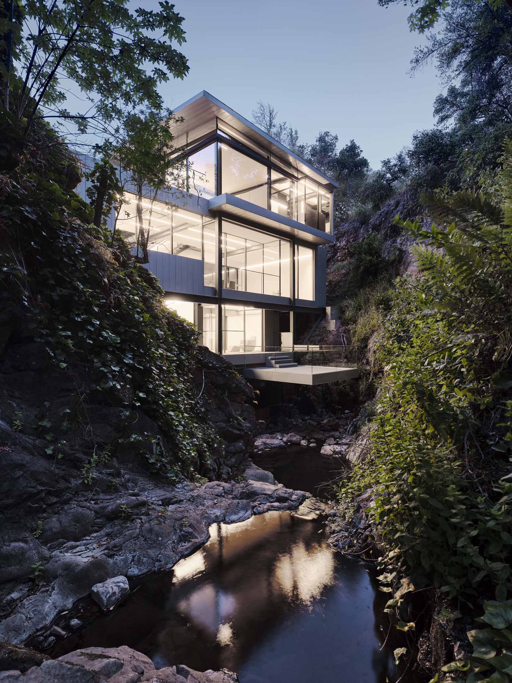 A modern home in California positioned between two hills and suspended over a creek.