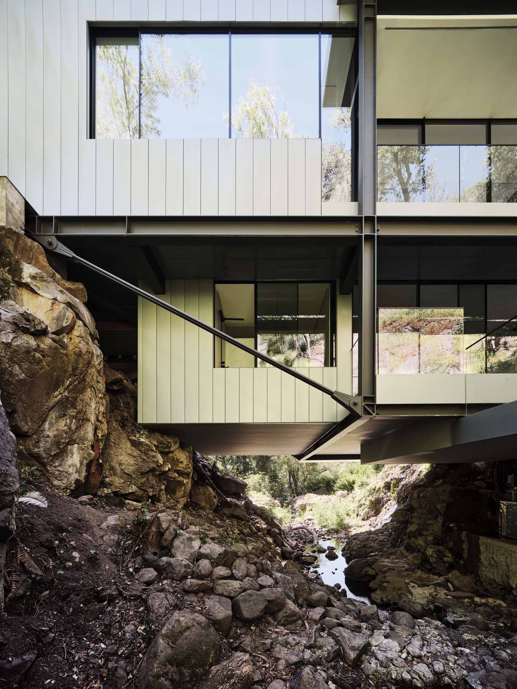 A modern home in California positioned between two hills and suspended over a creek.