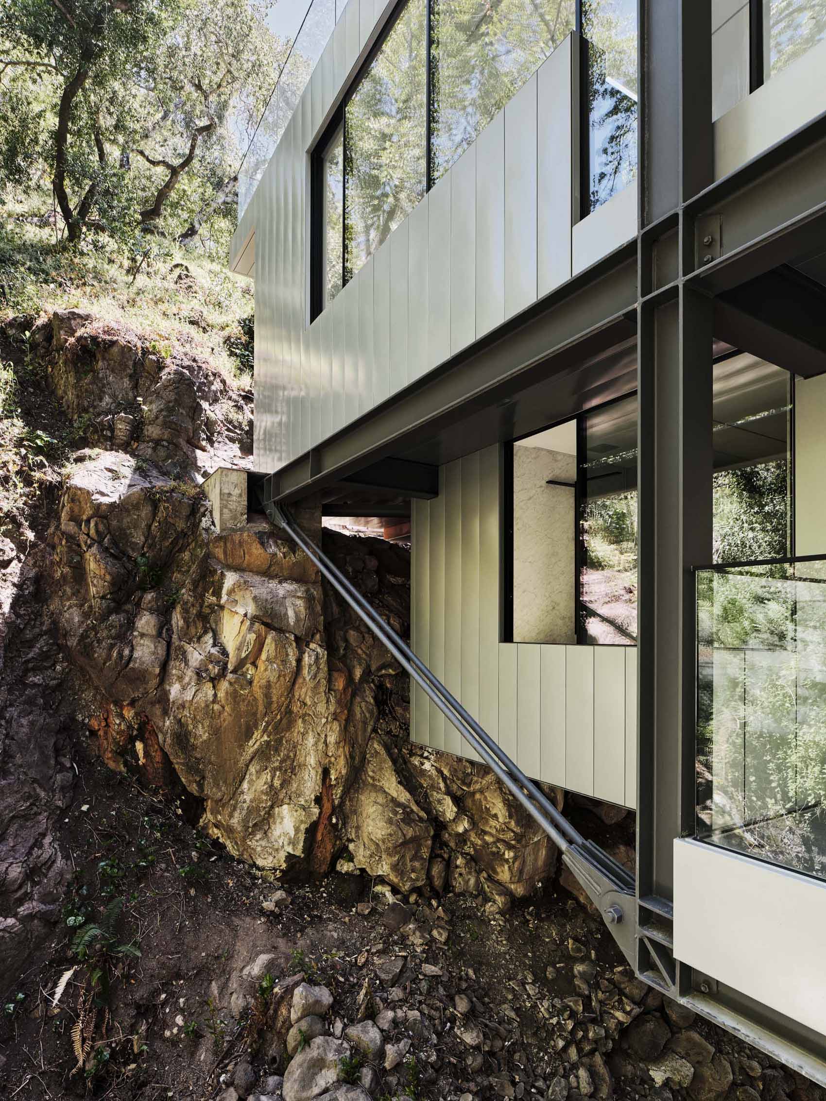 A modern home in California positioned between two hills and suspended over a creek.