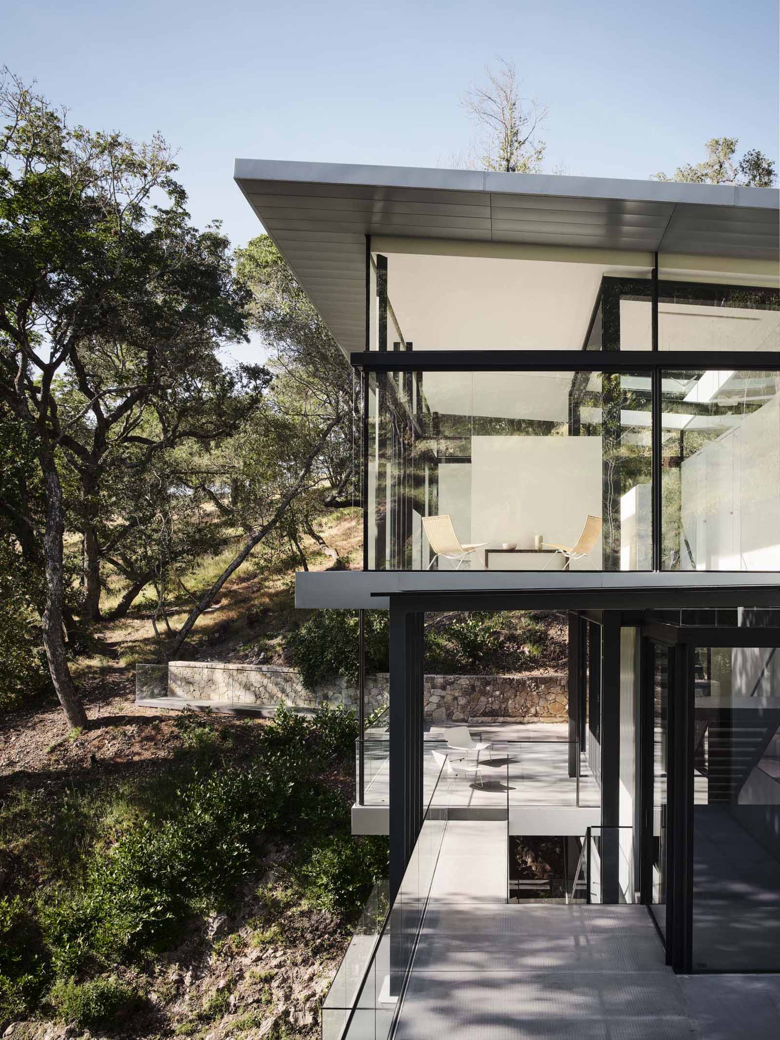 A modern home in California positioned between two hills and suspended over a creek.