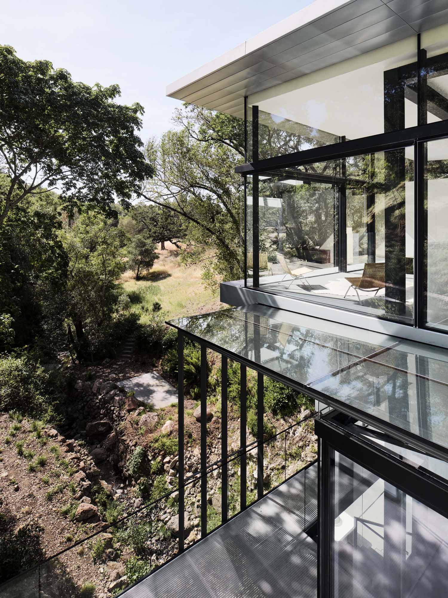 A modern home in California positioned between two hills and suspended over a creek.