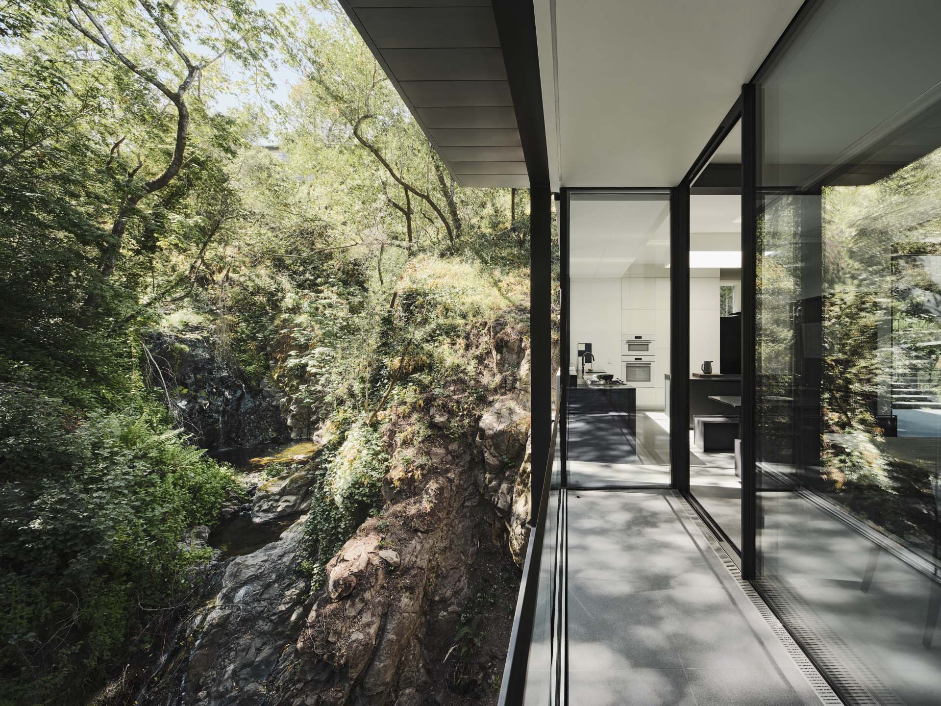 A modern home in California positioned between two hills and suspended over a creek.