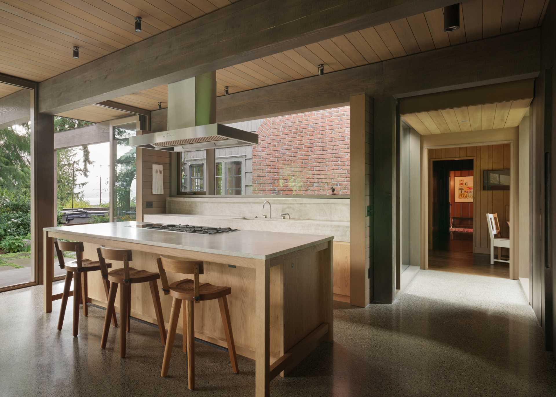 This kitchen interior has a polished concrete floor, stained knotty-oak cabinetry, and Quartzite countertops, including a custom stone kitchen sink. Appliances are fully integrated into the cabinetry. The space is organized around a large island.