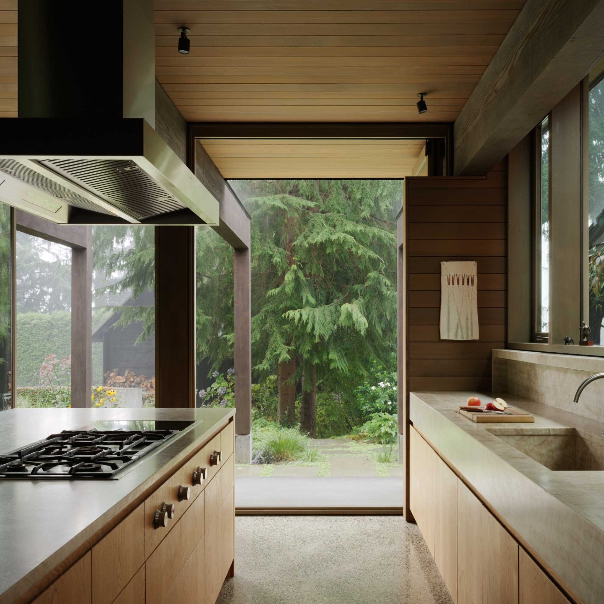 This kitchen interior has a polished concrete floor, stained knotty-oak cabinetry, and Quartzite countertops, including a custom stone kitchen sink. Appliances are fully integrated into the cabinetry. The space is organized around a large island.