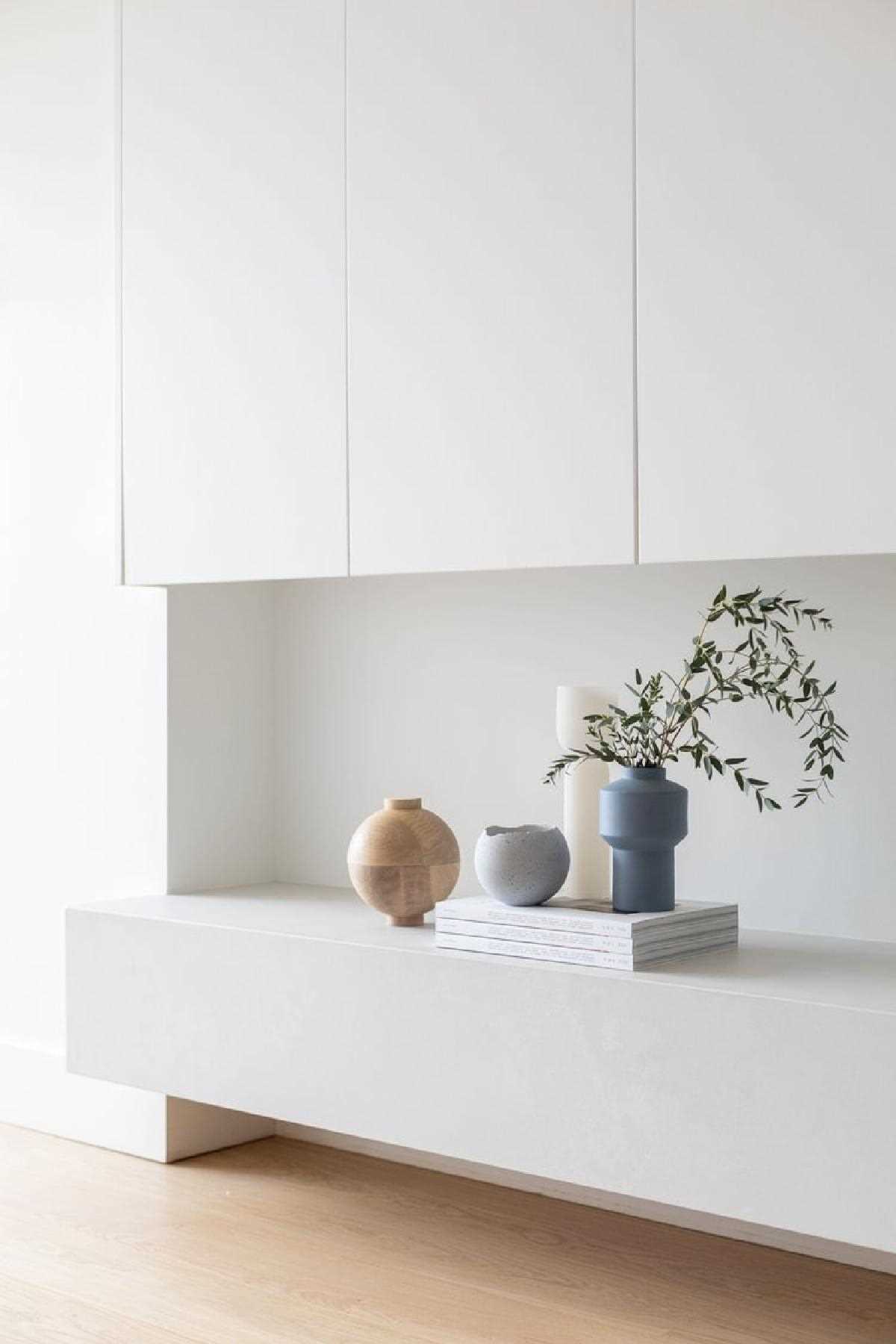 This modern living room has a concrete-hued quartz floating hearth. Bespoke living room millwork conceals the television, upholding a clean and uncluttered aesthetic