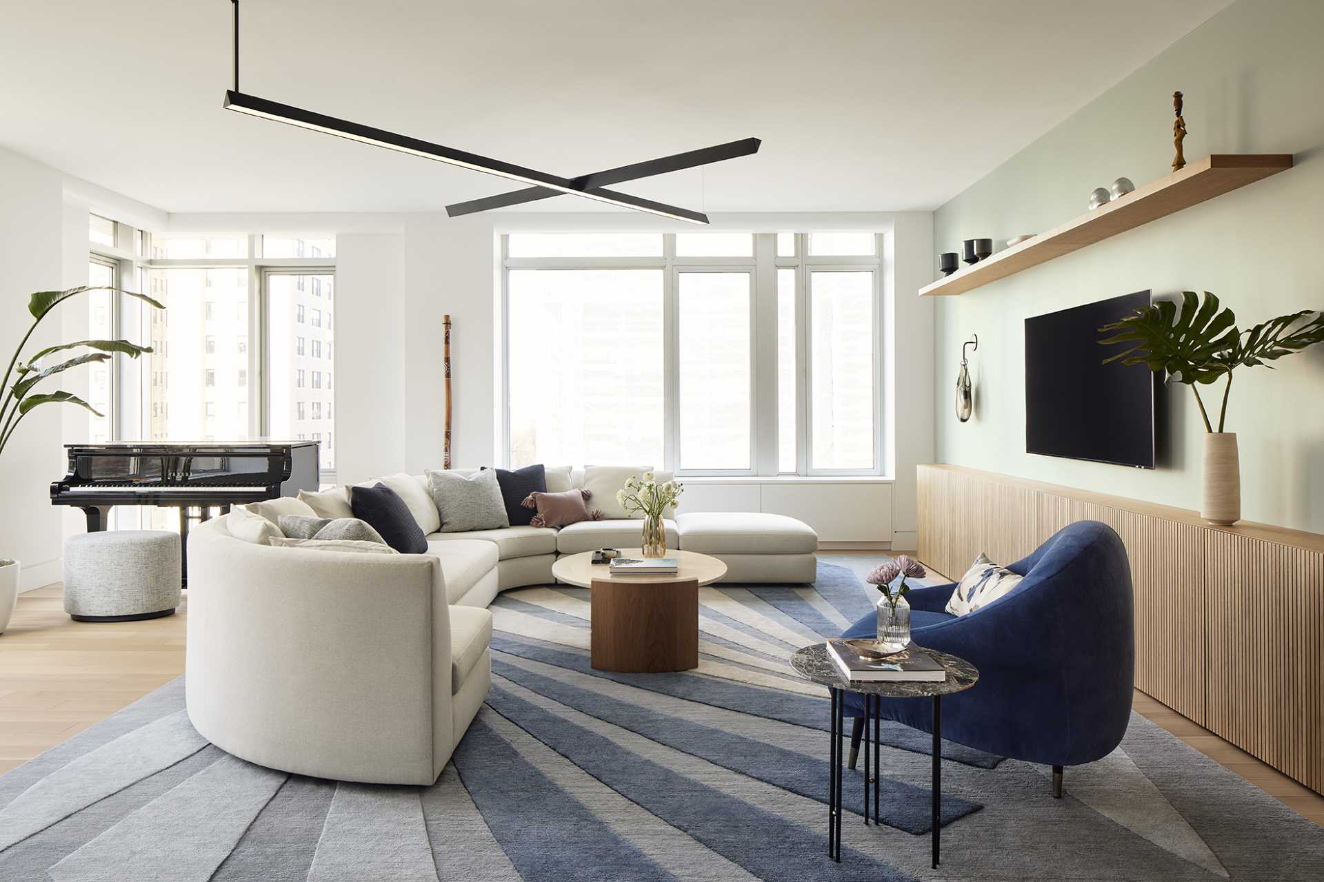 In the living room, custom-slatted white oak millwork has a fluted design, running horizontally along the base of one wall and extending into a vertically oriented, sculpturally rounded closet at the end.