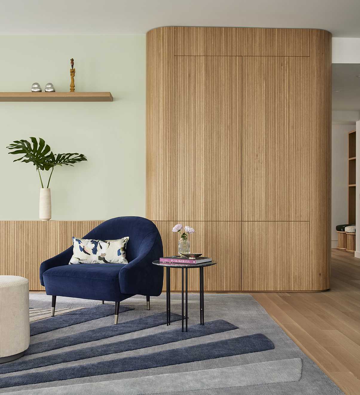 In the living room, custom-slatted white oak millwork has a fluted design, running horizontally along the base of one wall and extending into a vertically oriented, sculpturally rounded closet at the end.