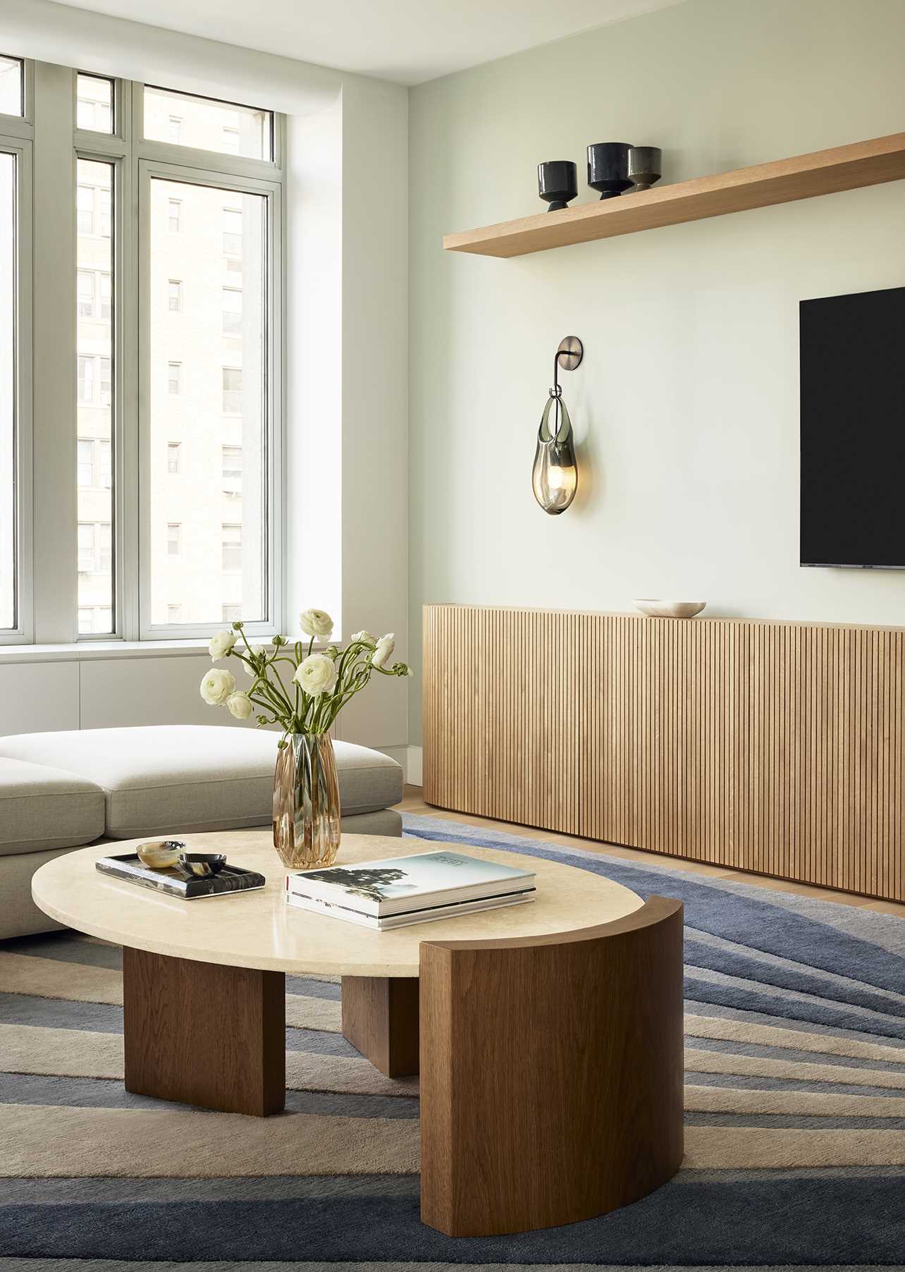 In the living room, custom-slatted white oak millwork has a fluted design, running horizontally along the base of one wall and extending into a vertically oriented, sculpturally rounded closet at the end.