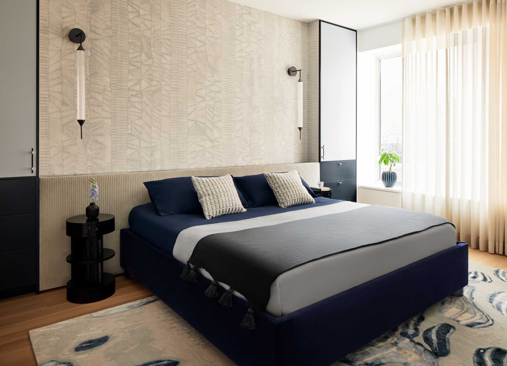 A modern primary bedroom with deep blues, textures, and subtle wallpaper.