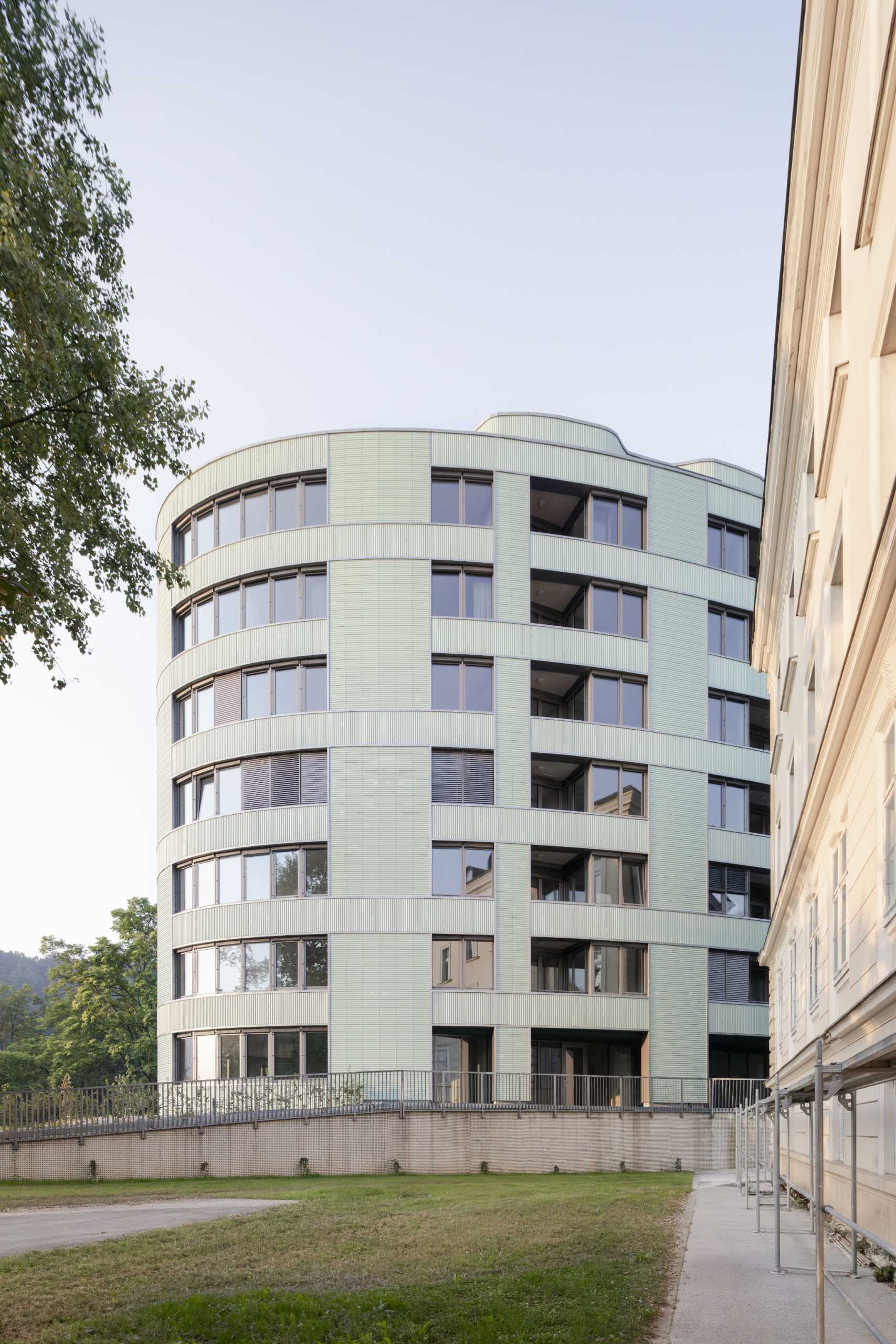 A modern residential building with undulating balconies and a facade covered in mint green tiles.