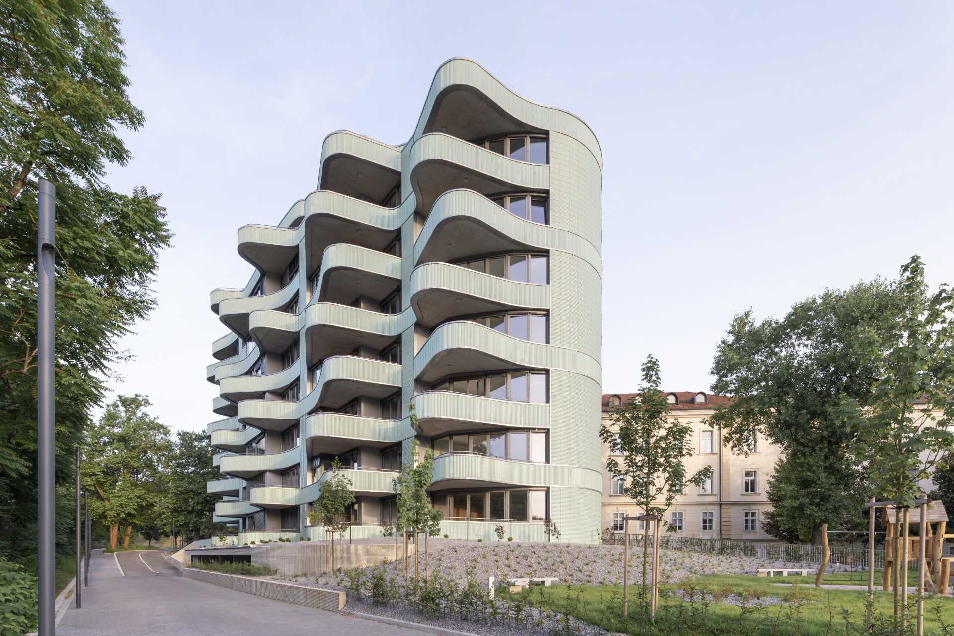 A modern residential building with undulating balconies and a facade covered in mint green tiles.