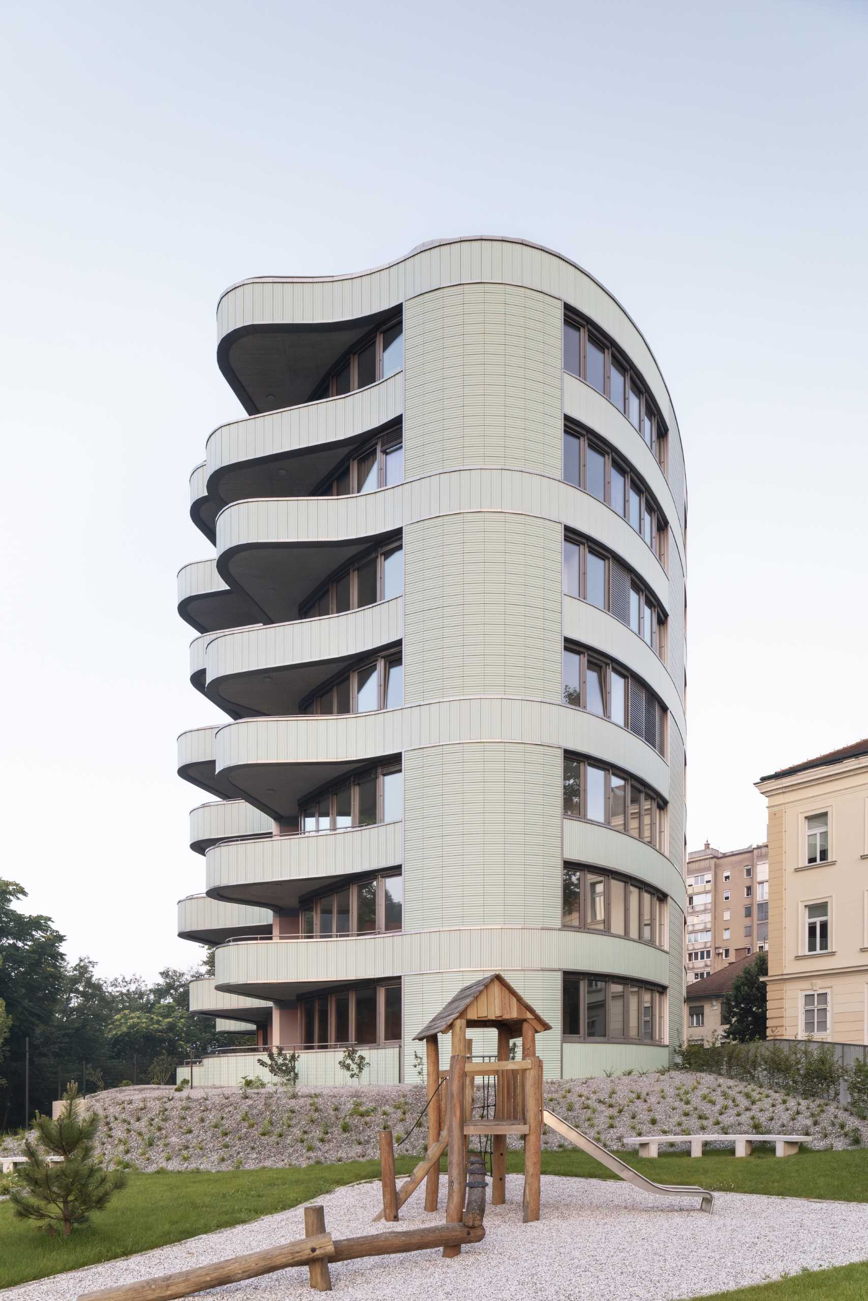 A modern residential building with undulating balconies and a facade covered in mint green tiles.