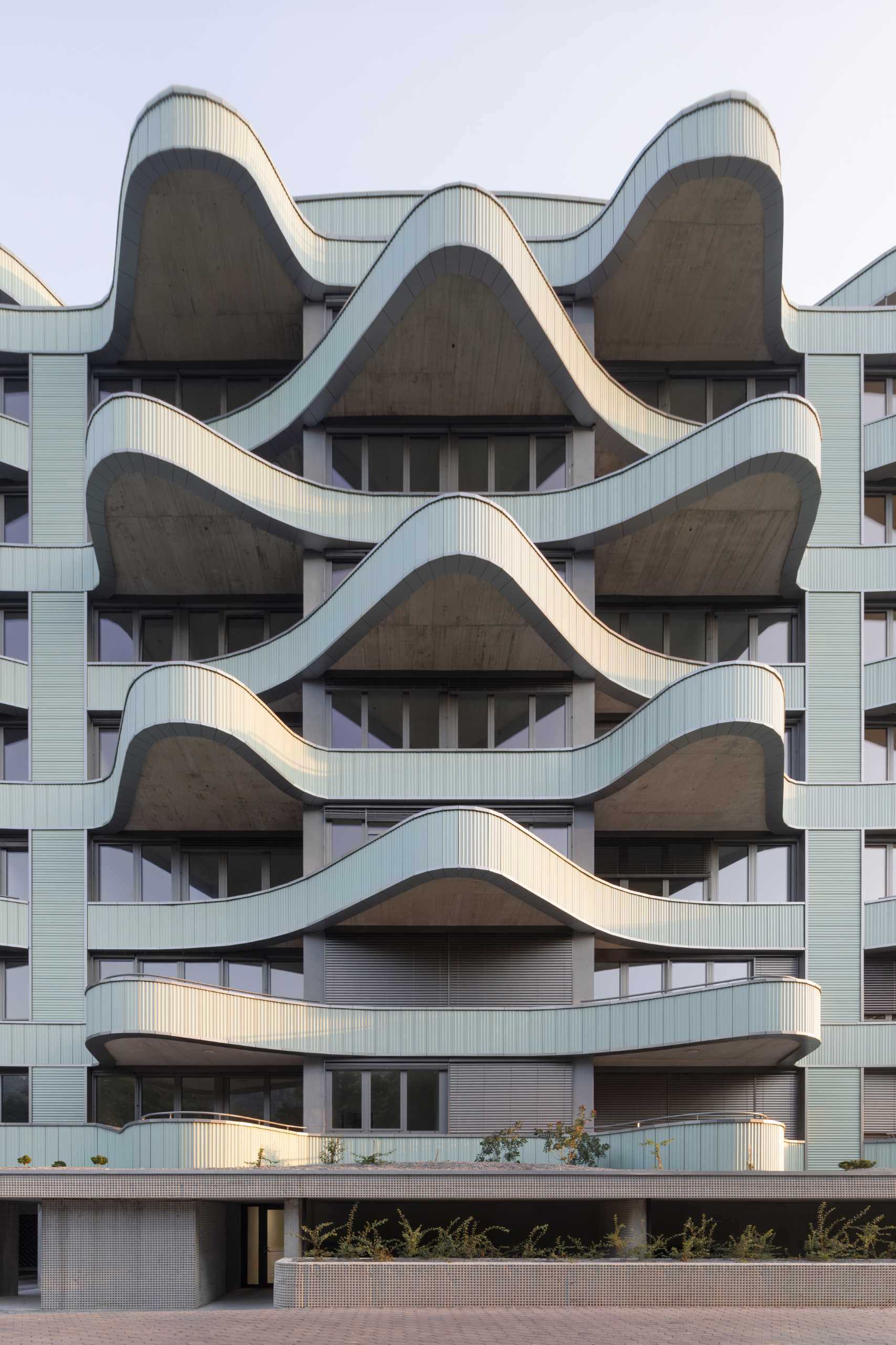 A modern residential building with undulating balconies and a facade covered in mint green tiles.