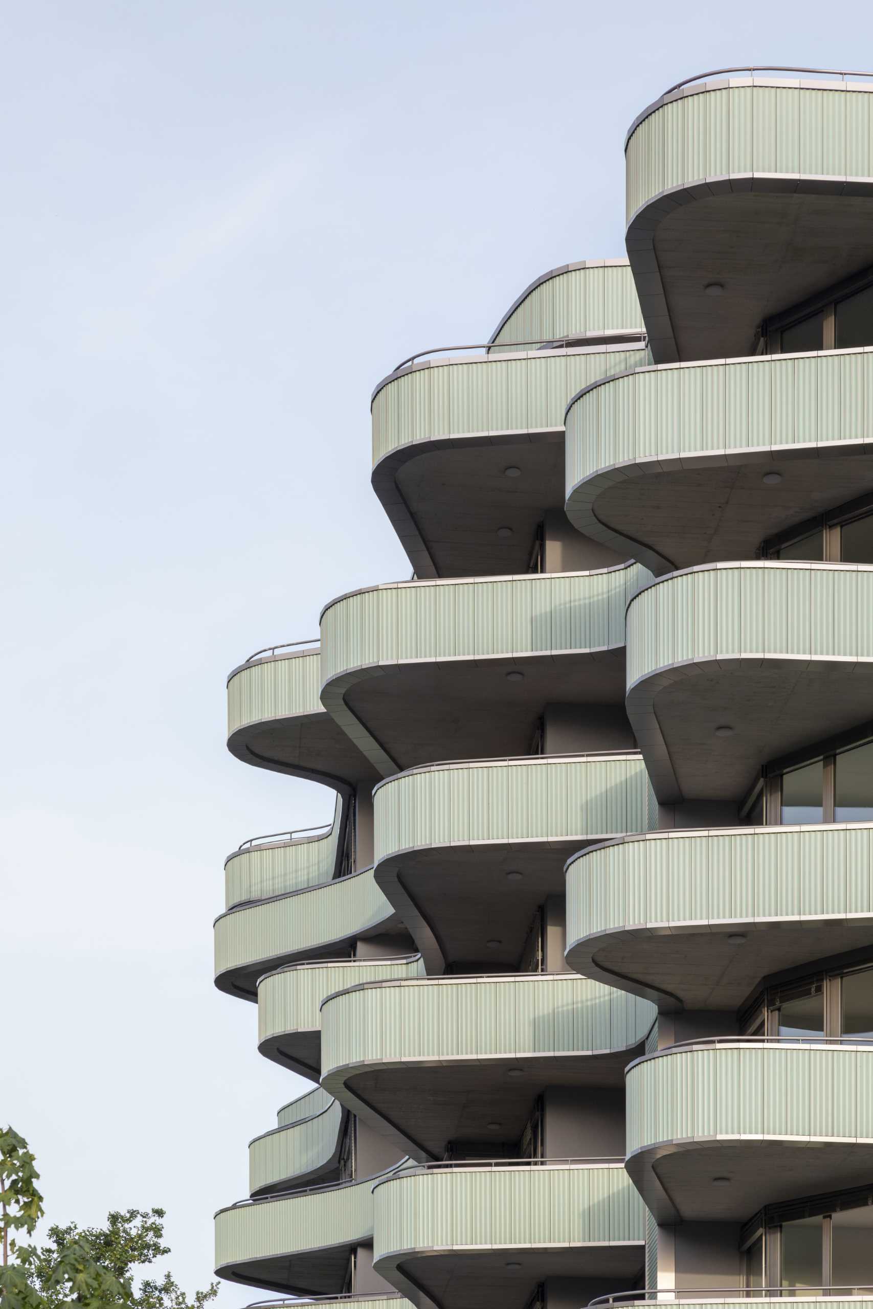 A modern residential building with undulating balconies and a facade covered in mint green tiles.