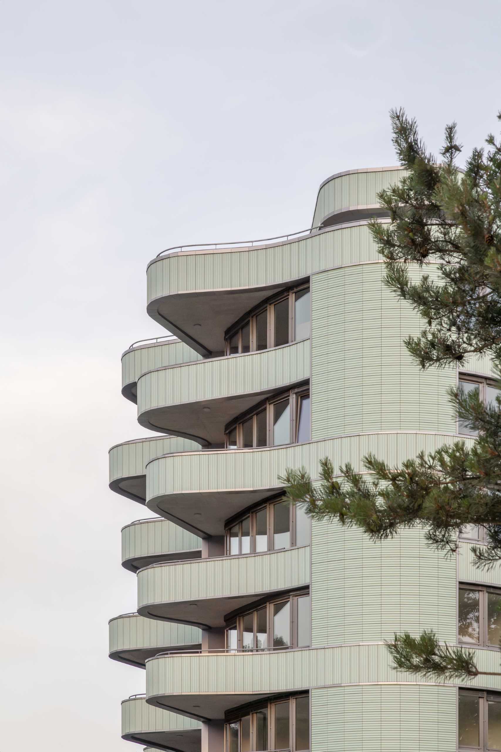 A modern residential building with undulating balconies and a facade covered in mint green tiles.