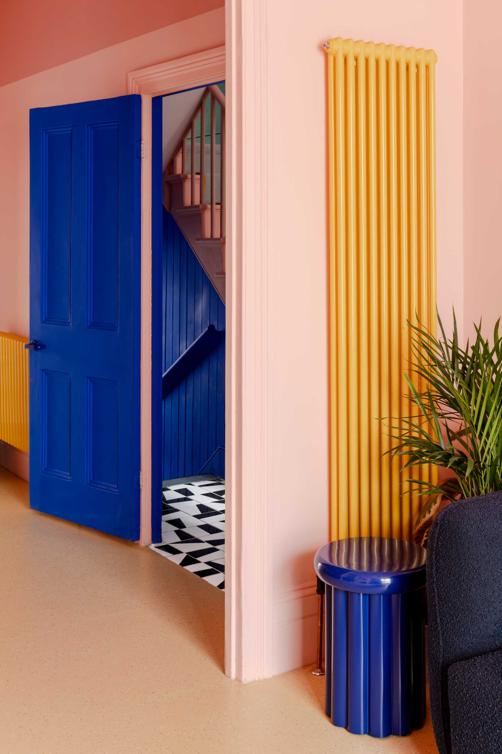 The living room features a soft pastel pink design with bold blue and yellow accents, as well as a natural linoleum floor.