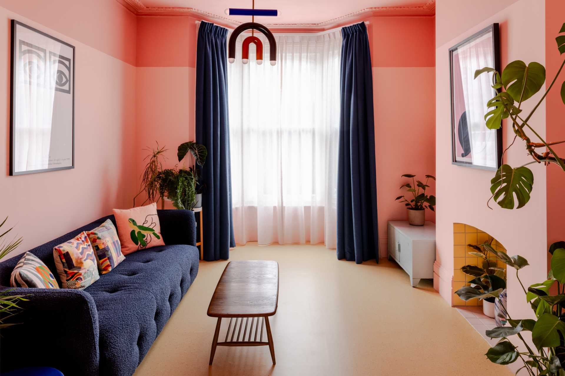 The living room features a soft pastel pink design with bold blue and yellow accents, as well as a natural linoleum floor.