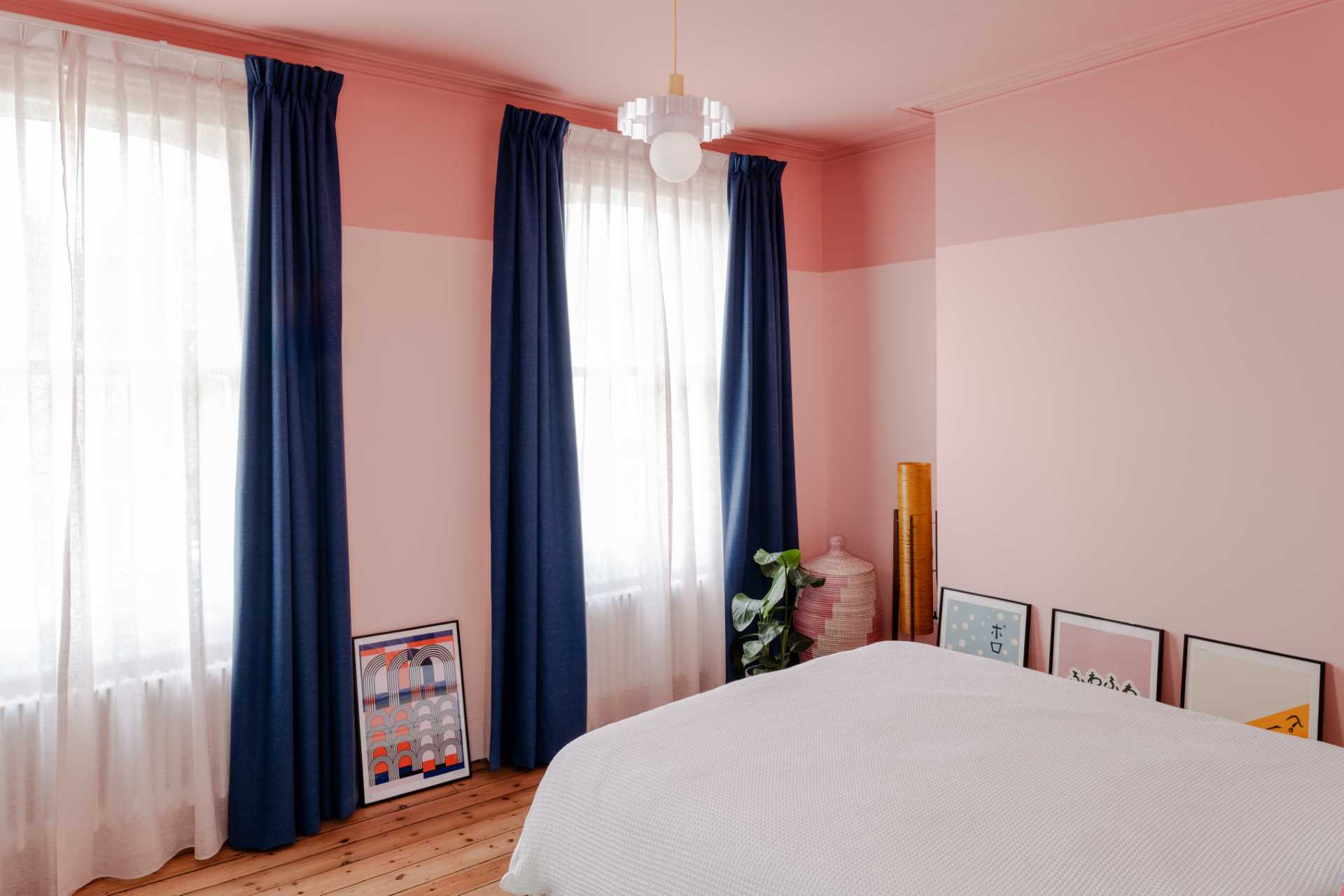 In this primary bedroom, two-tone pink walls provide a backdrop for the deep navy blue curtains.