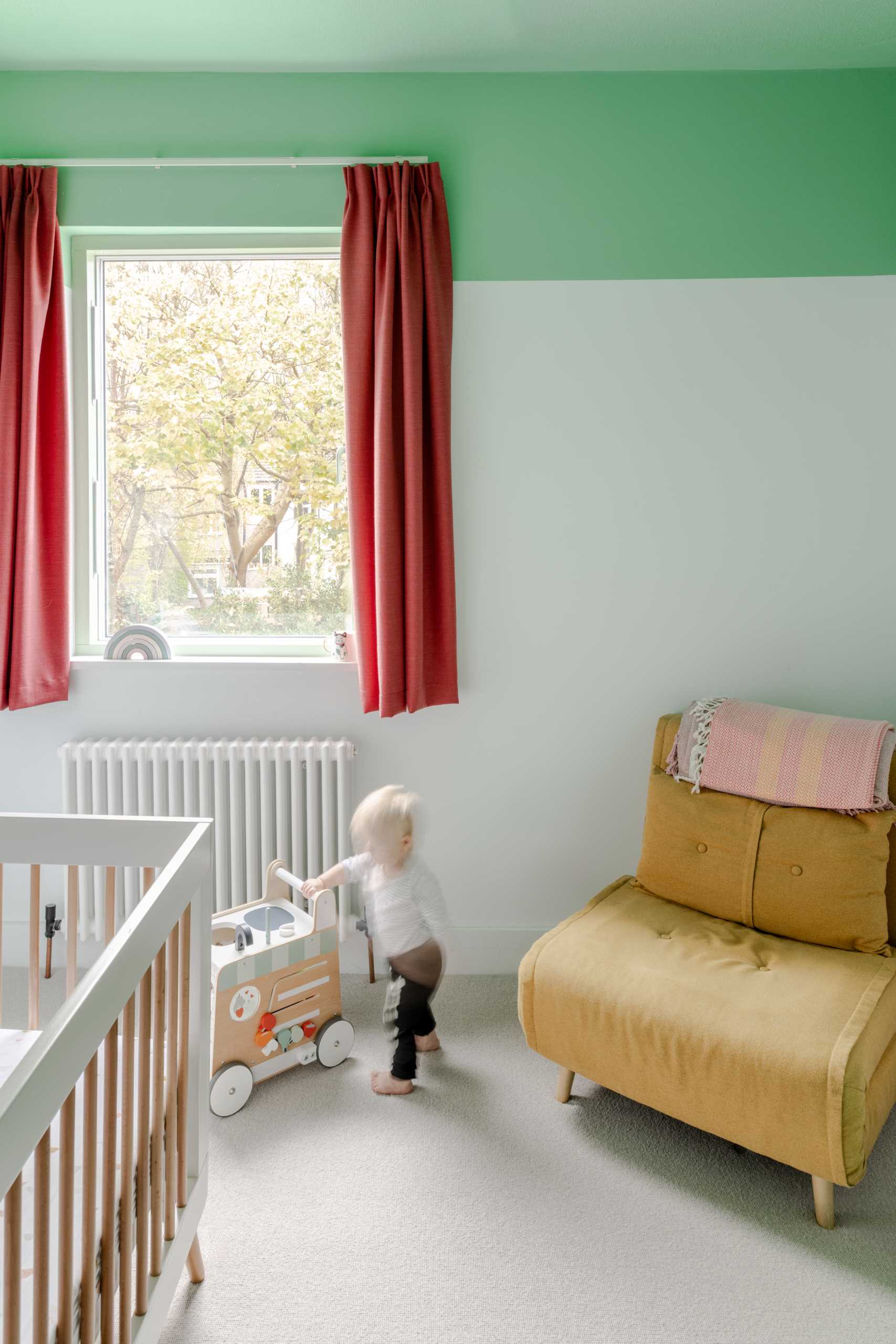 In this bedroom, there are green and white walls with a pop of contrasting color in the form of curtains.