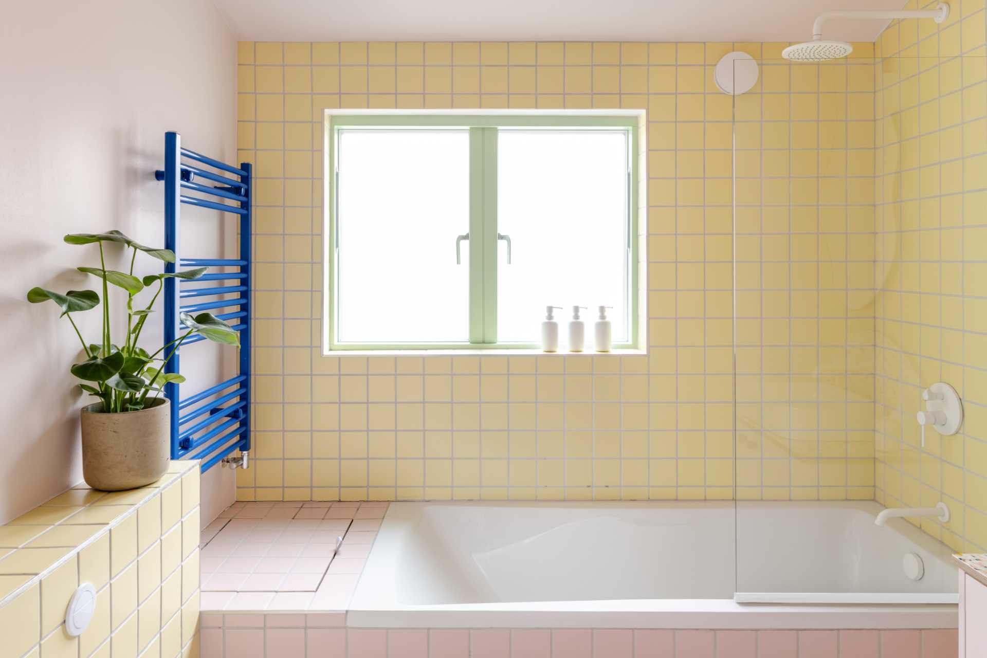 In this bathroom, square yellow tiles cover the walls and meet the pink tiles that wrap around the bathtub, while an organically shaped mirror adds a fun element.